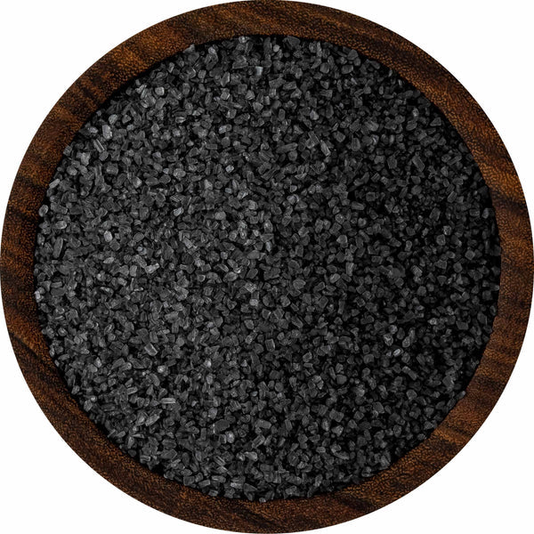 Wooden bowl filled with black salt on a white background
