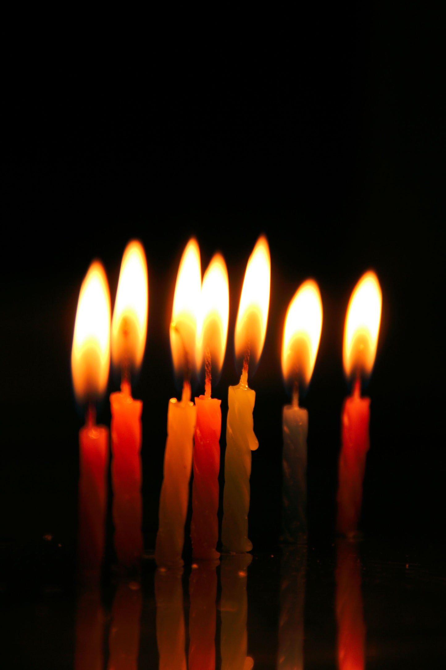 Birthday candles lit in a row on a black background.