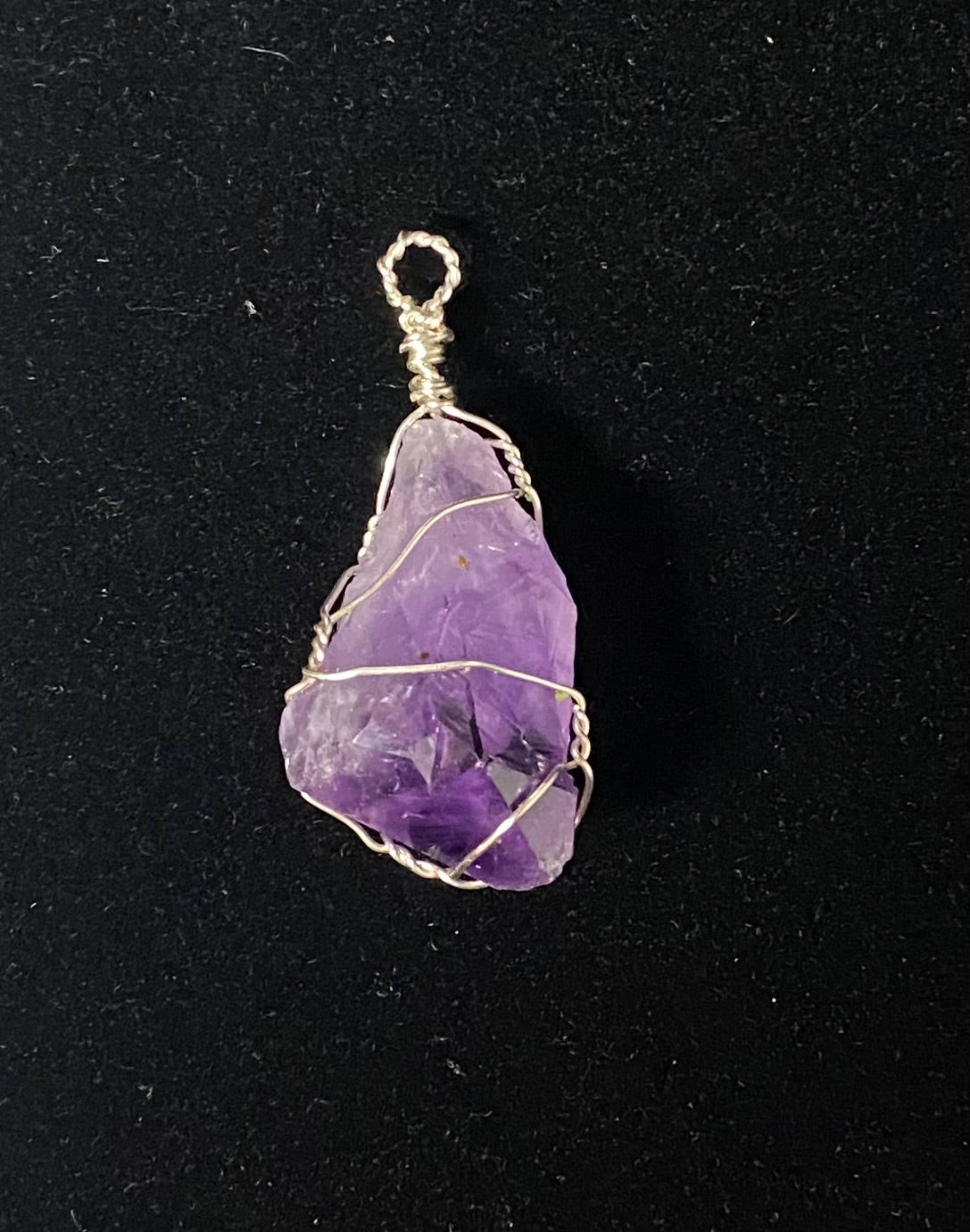 A raw purple amethyst stone pendant wrapped in gold-toned wire, shown against a black background.
