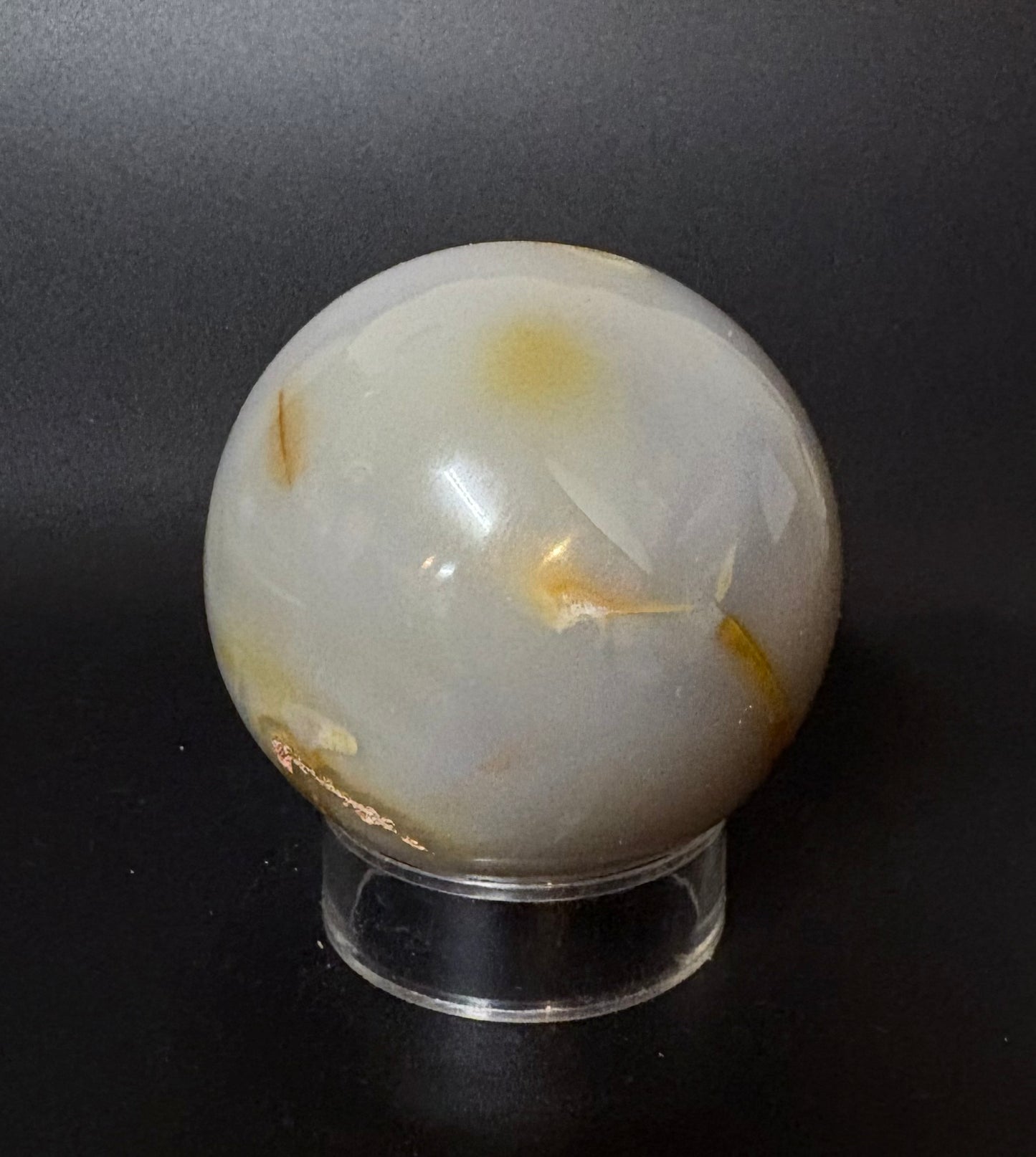 Blue Chalcedony sphere with gold inclusions on a clear stand against a black background
