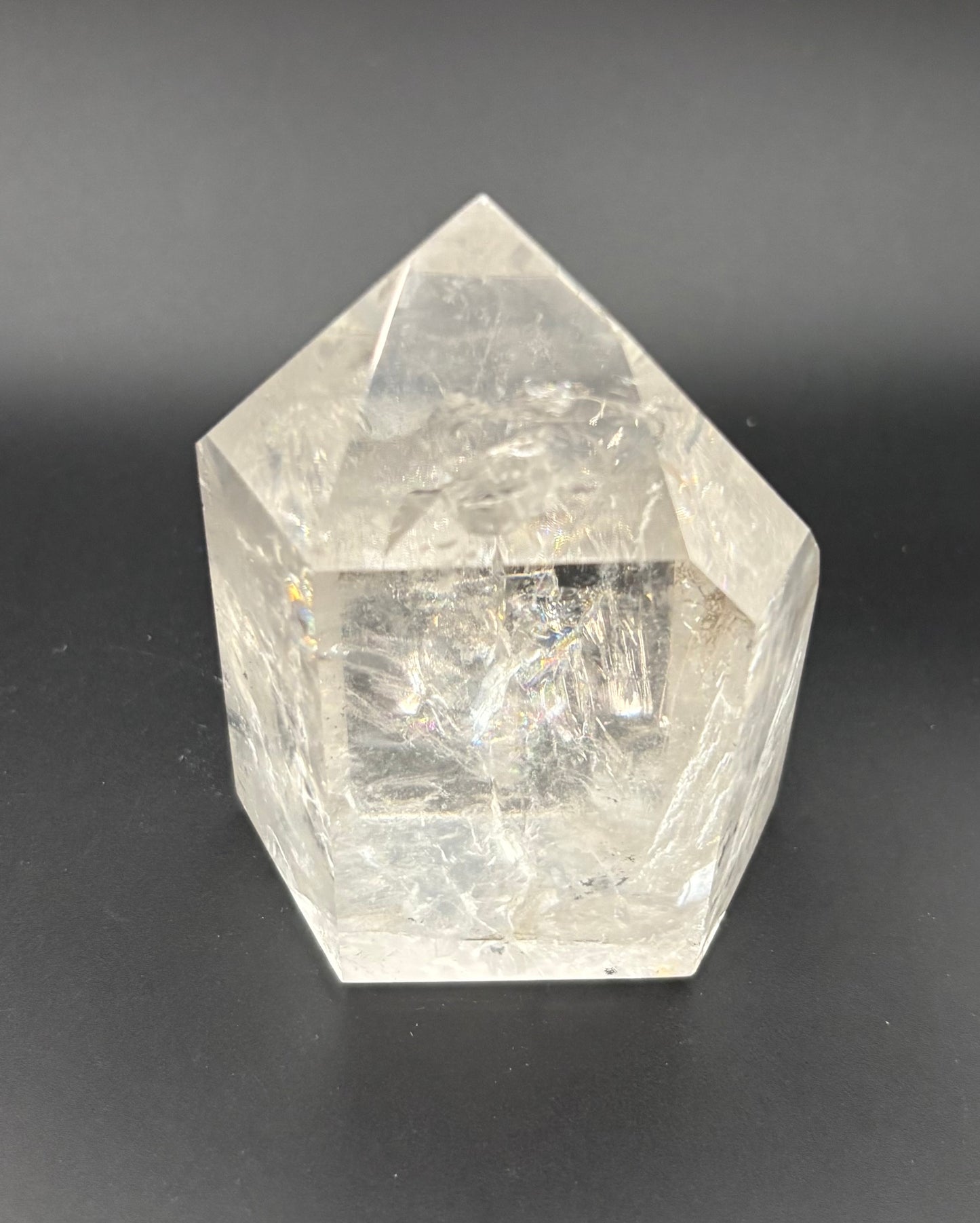A clear faceted quartz crystal point, with natural internal inclusions, photographed on a dark gray background.