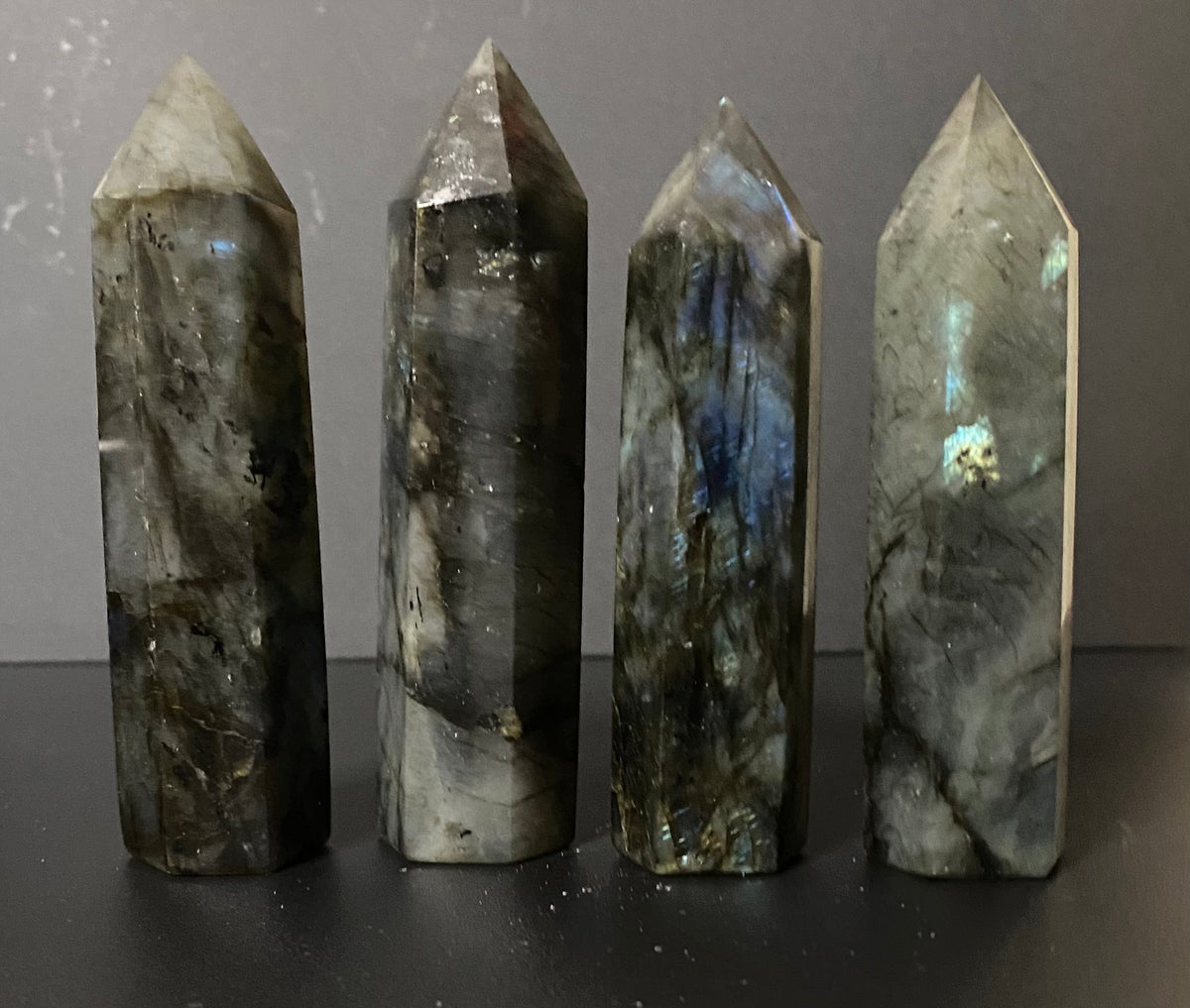 Four polished labradorite crystal points of varying heights standing upright on a dark surface against a gray background.