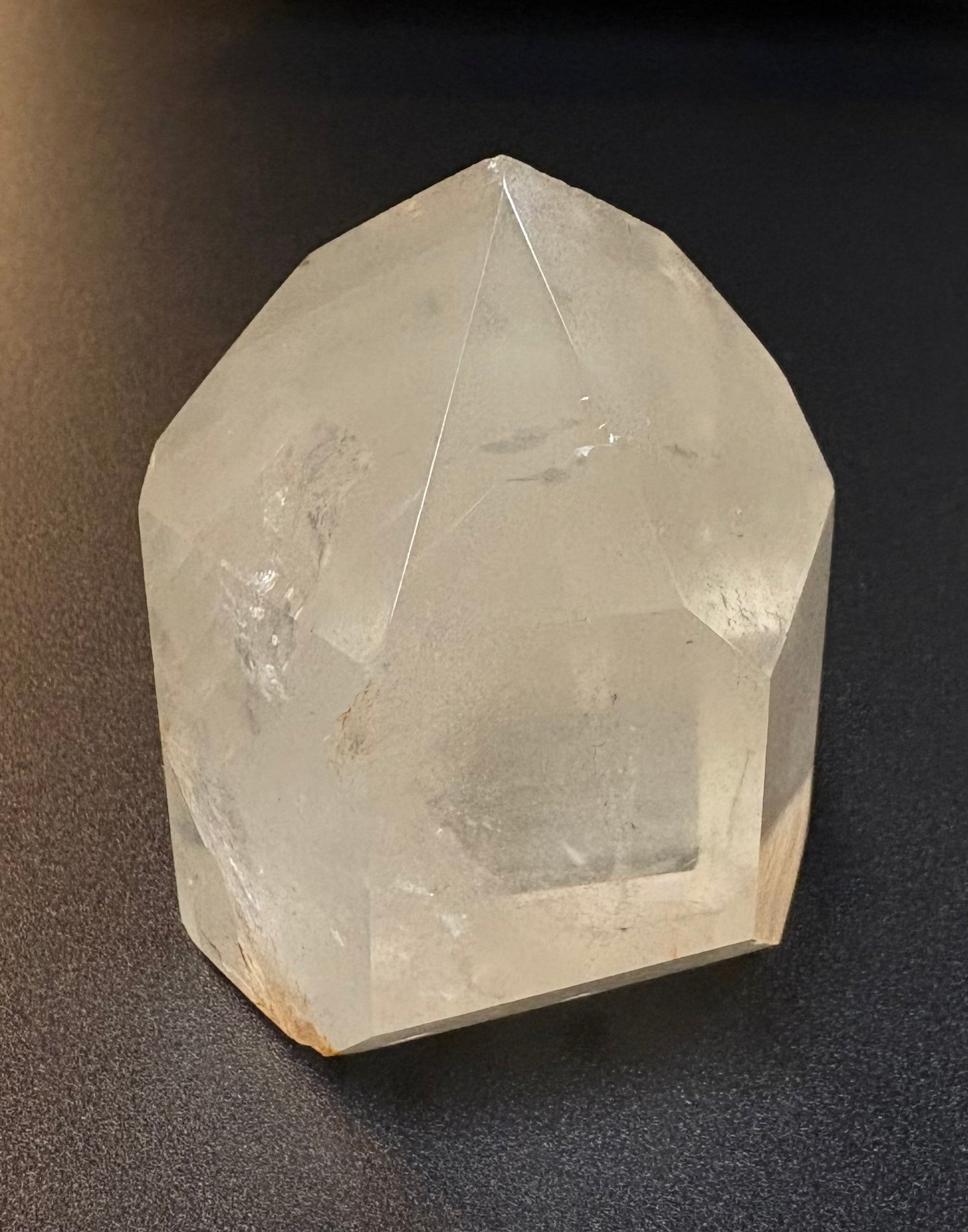 A natural clear quartz crystal point with geometric facets, resting on a dark textured surface.