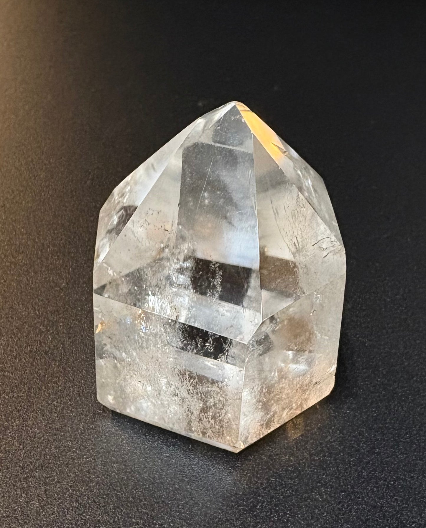 A clear quartz crystal point with natural inclusions, photographed on a dark textured background.