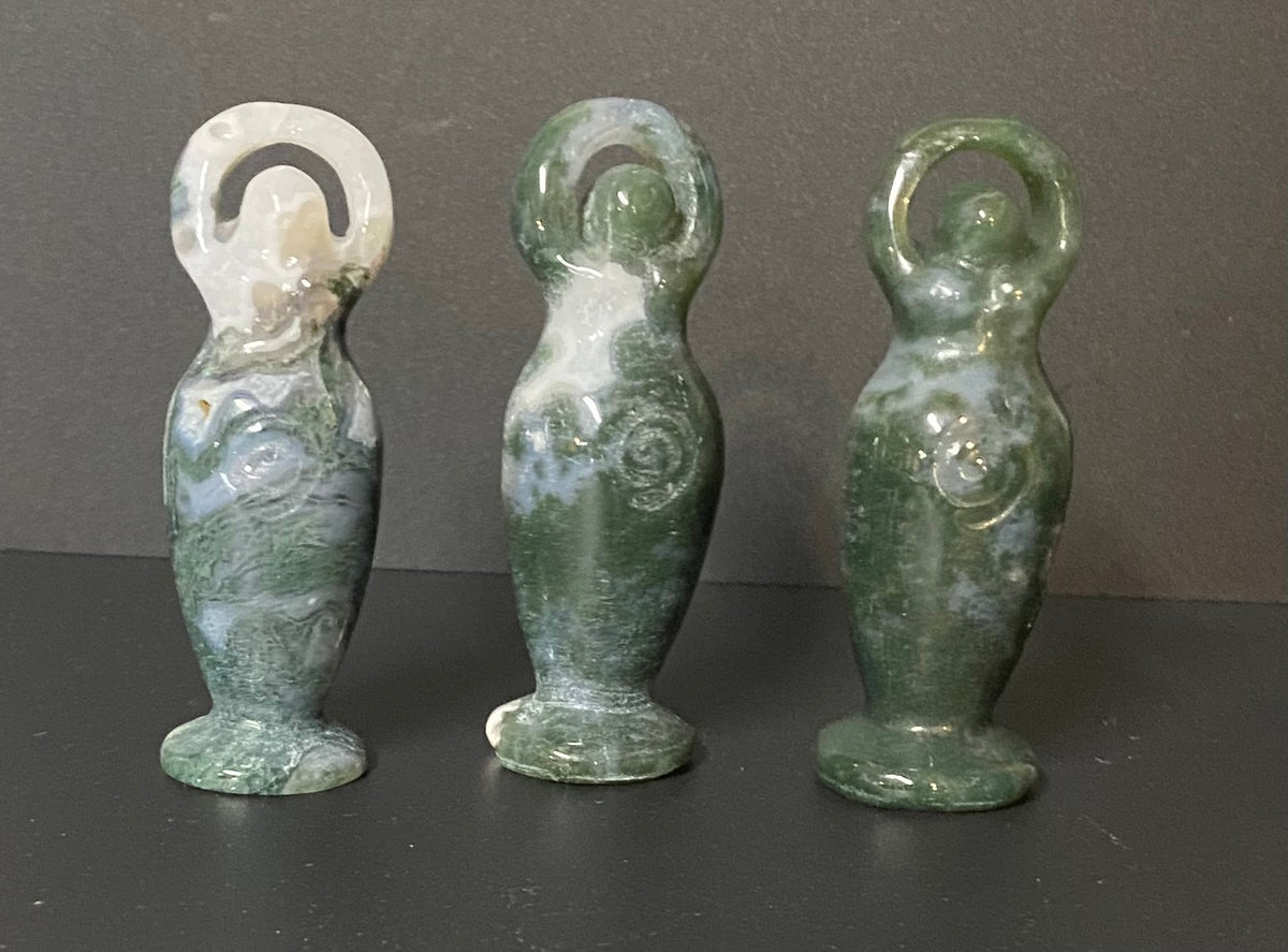 Three small green stone Moss Agate figurines with white marbled patterns, standing on a dark surface against a dark gray background.