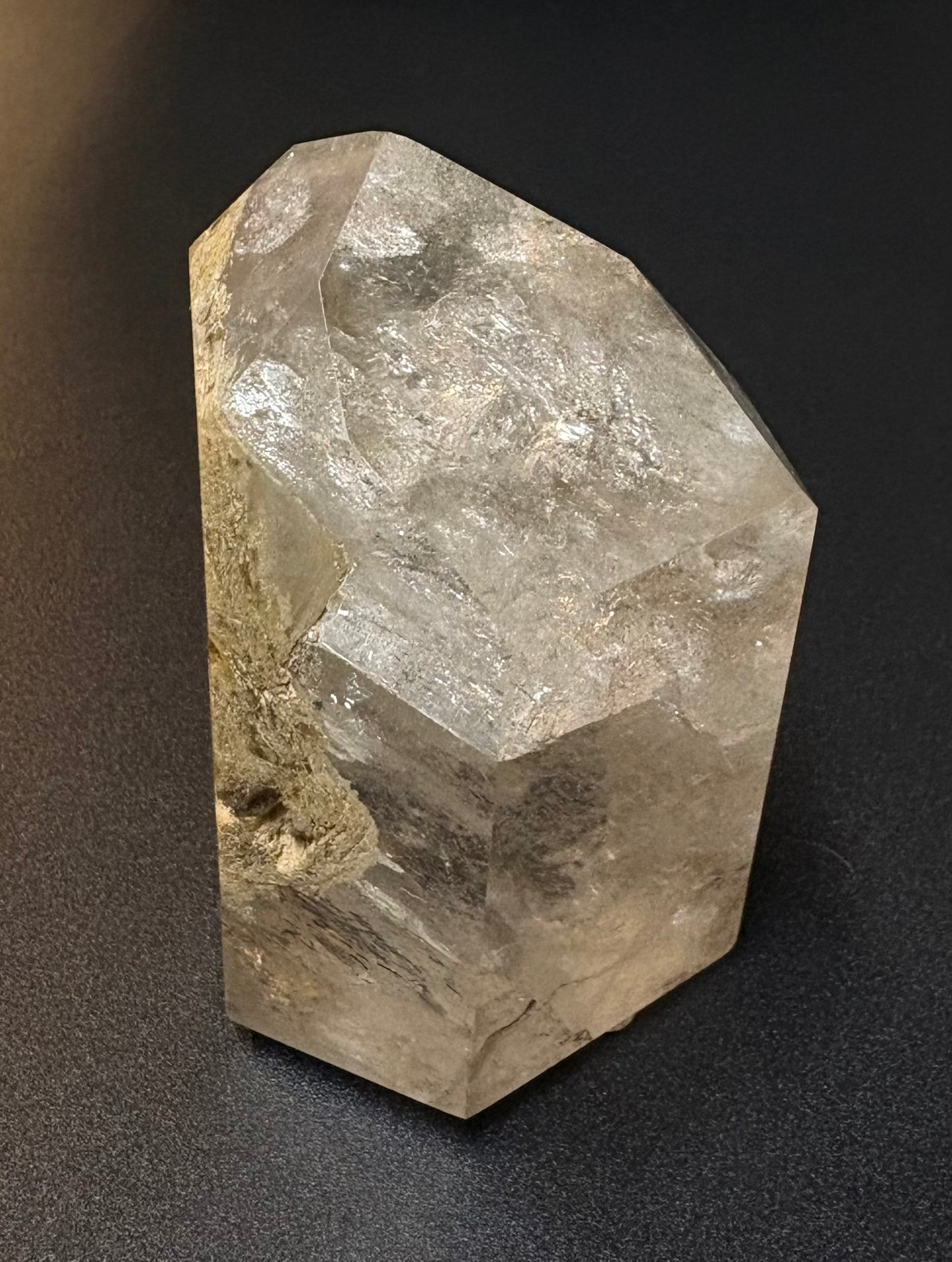 A raw, faceted quartz crystal cluster with natural inclusions, displayed on a dark textured background.