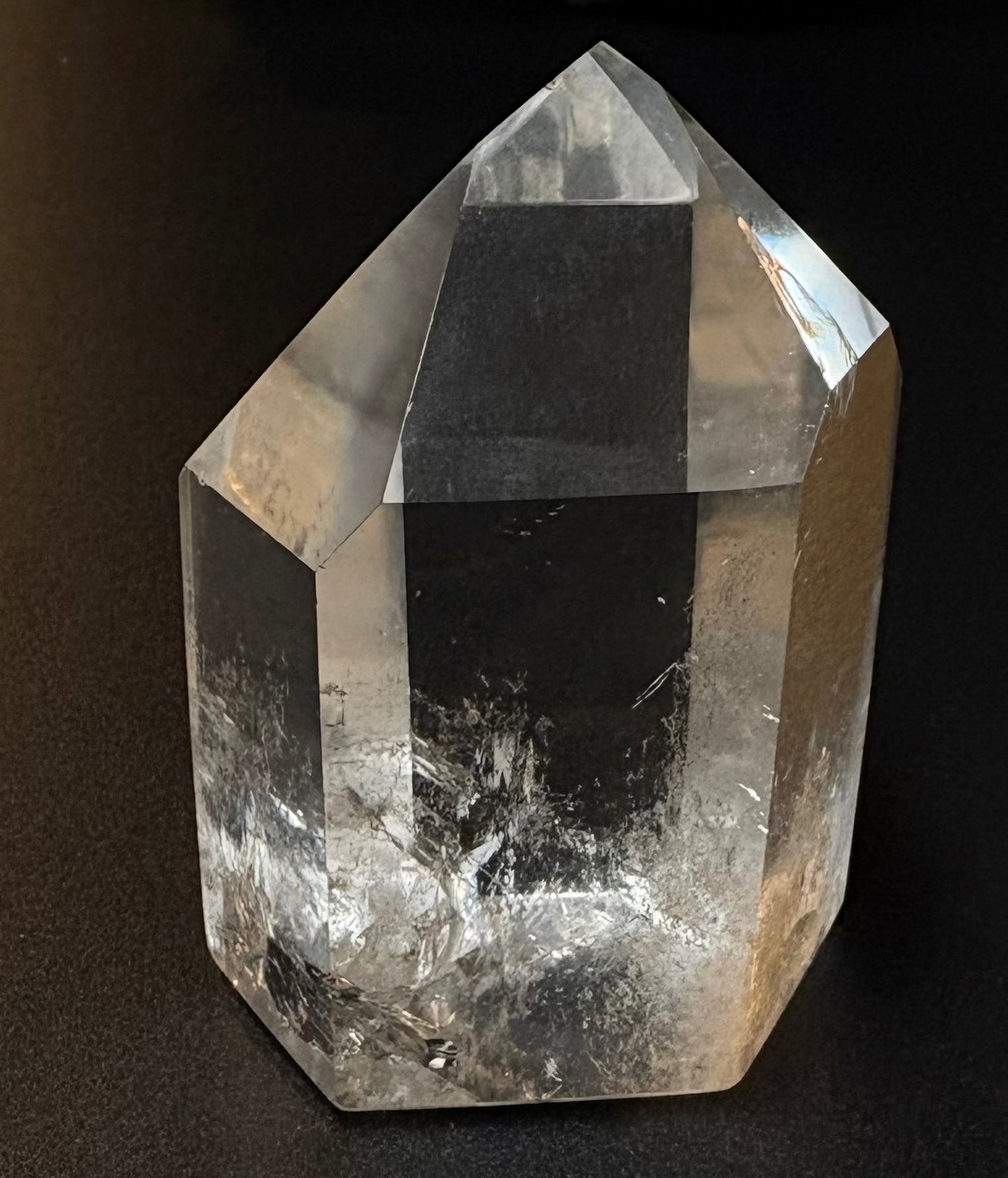 A clear quartz crystal point with natural inclusions, photographed against a dark black background.