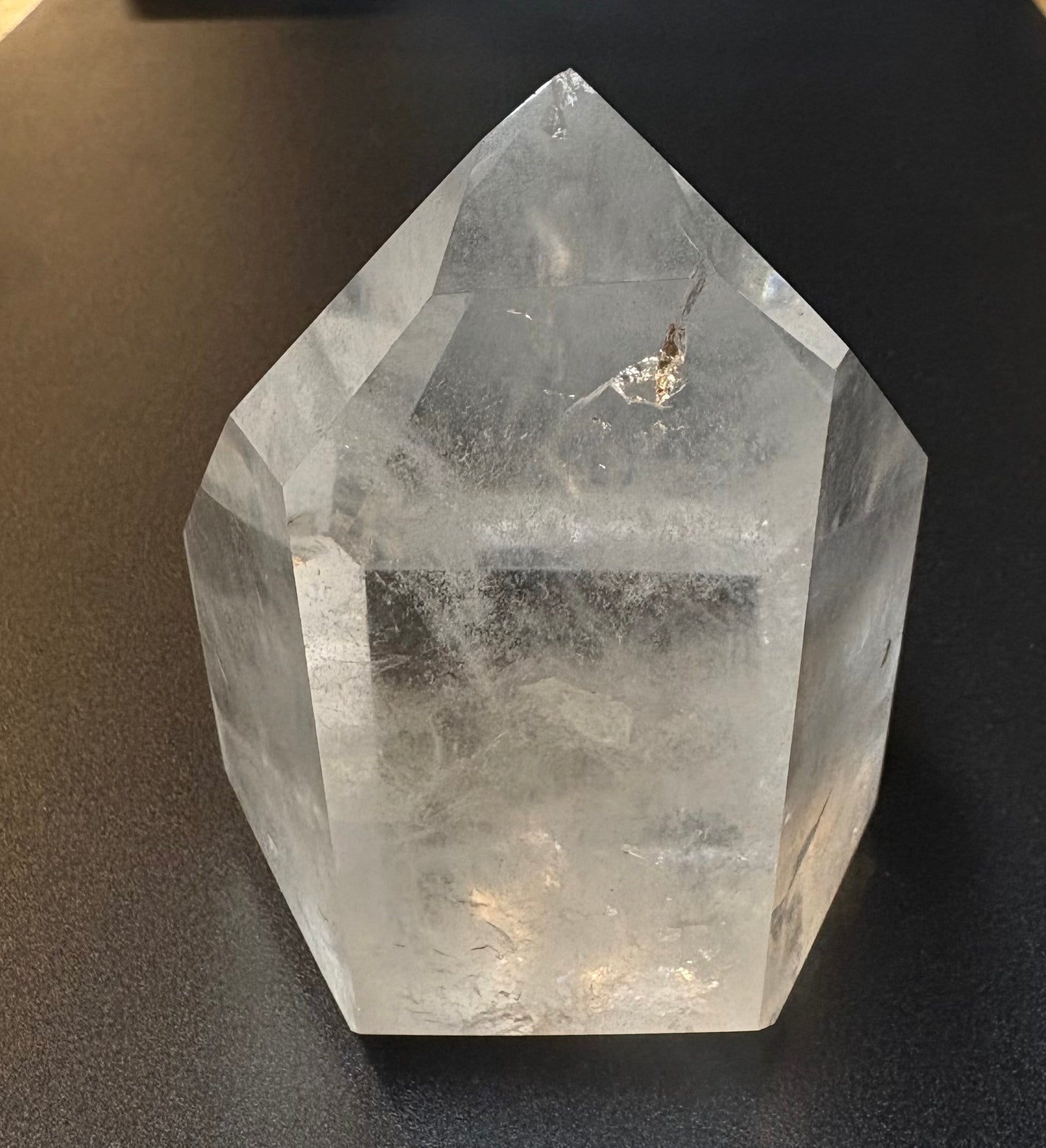 A clear quartz crystal point tower with natural inclusions and fractures, photographed on a dark textured surface.