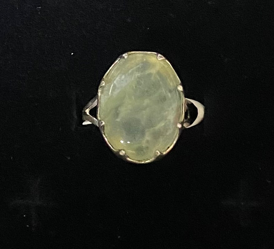 A vintage-style silver ring featuring an oval, milky pale green stone, photographed against a solid black background.