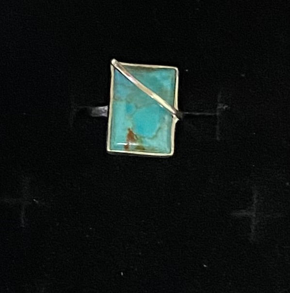 A rectangular turquoise stone ring with a Sterling Silver bezel and diagonal wrap detail, shown on a black background.