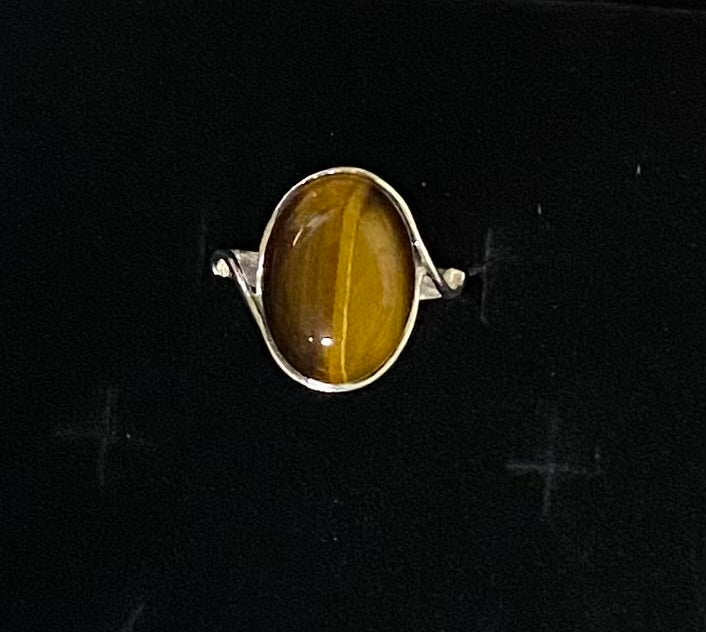 A silver ring featuring an oval cabochon gemstone with a distinct golden-brown vertical band, set against a dark black background.