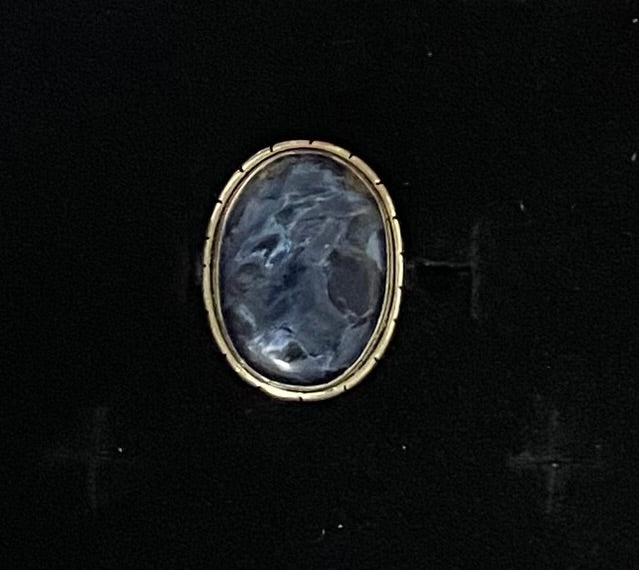 An oval vintage-style ring featuring a dark blue-gray carved stone in a sterling silver setting, shown on a black background.