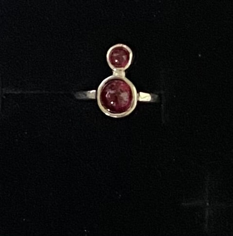 A sterling silver ring featuring two oval red gemstones stacked vertically, displayed on a black background.