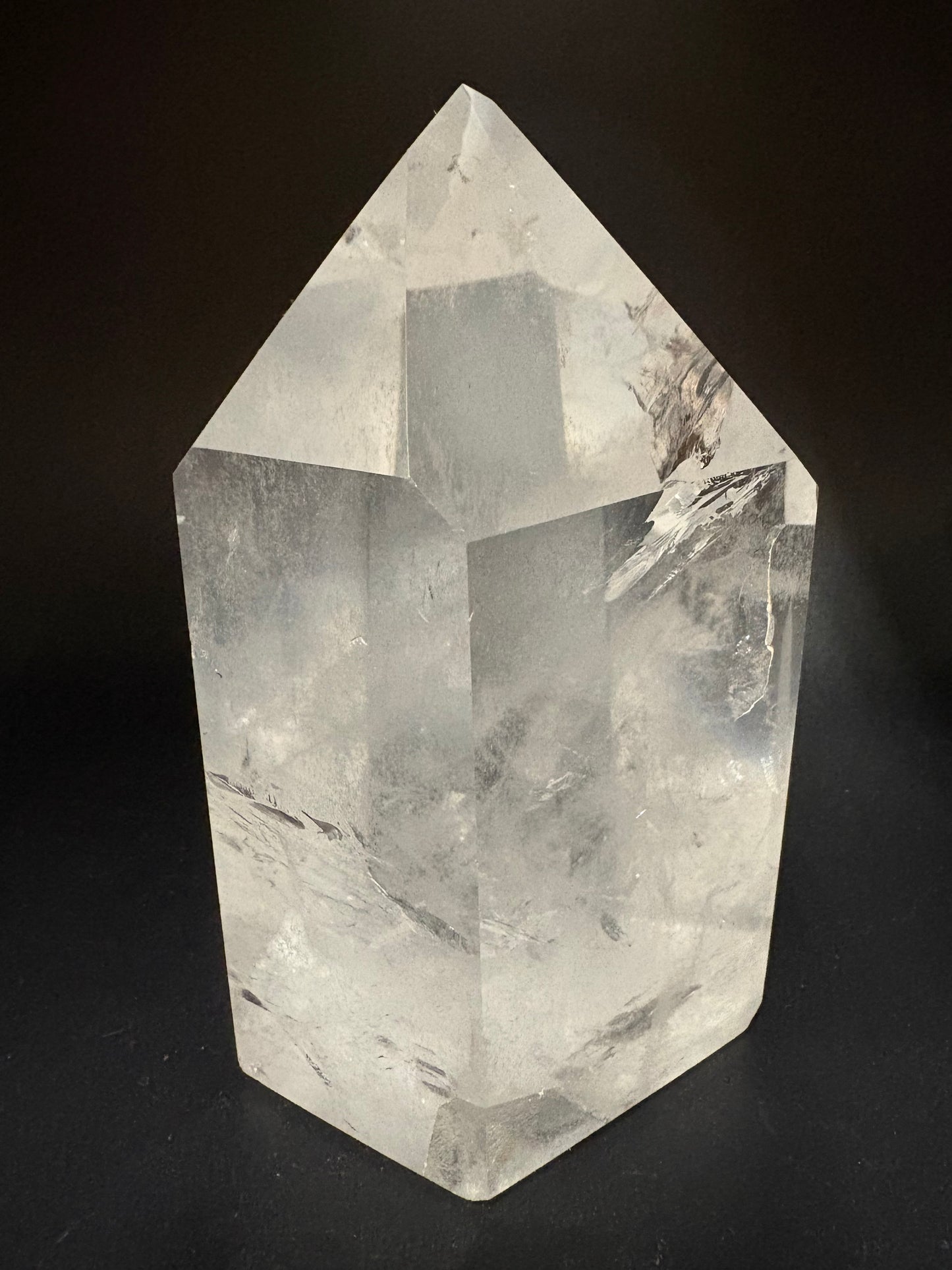 A natural clear quartz crystal point with internal inclusions, displayed on a solid black background.