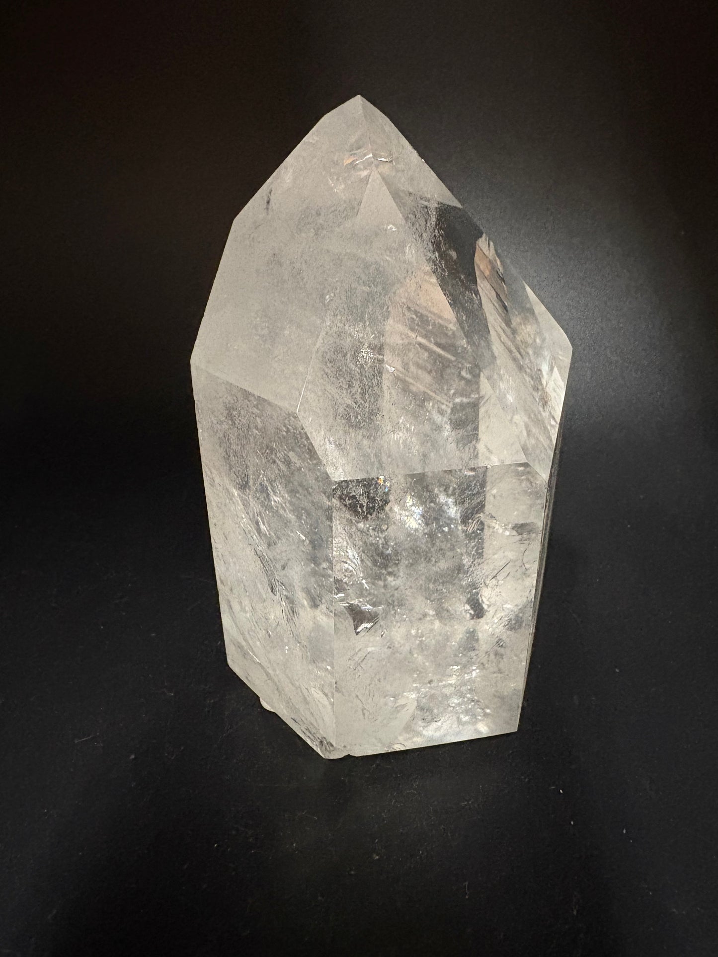 A raw, unpolished clear quartz crystal point with natural inclusions, displayed on a dark black background.