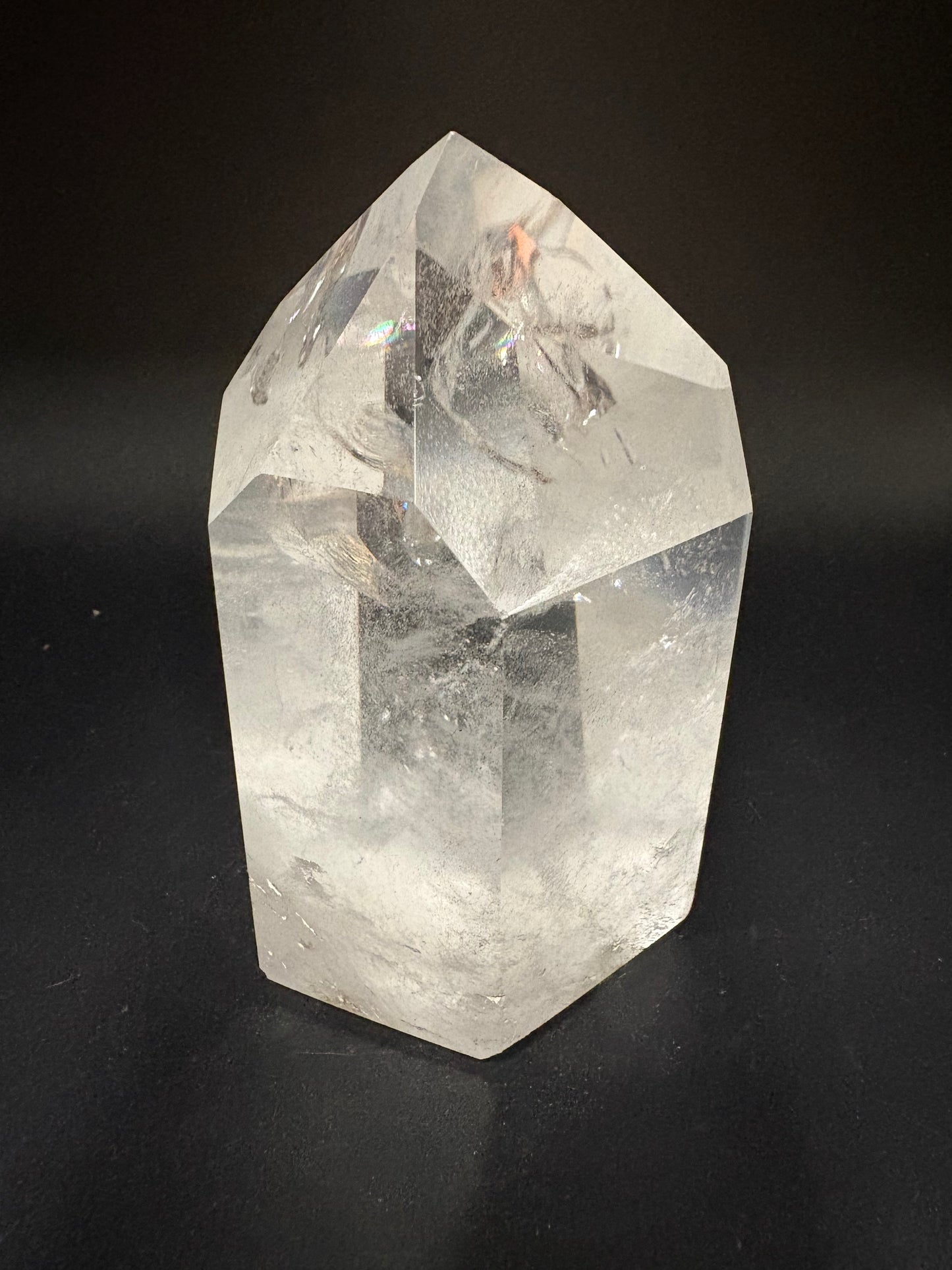 A faceted clear quartz crystal point with natural inclusions, displayed on a dark black background.