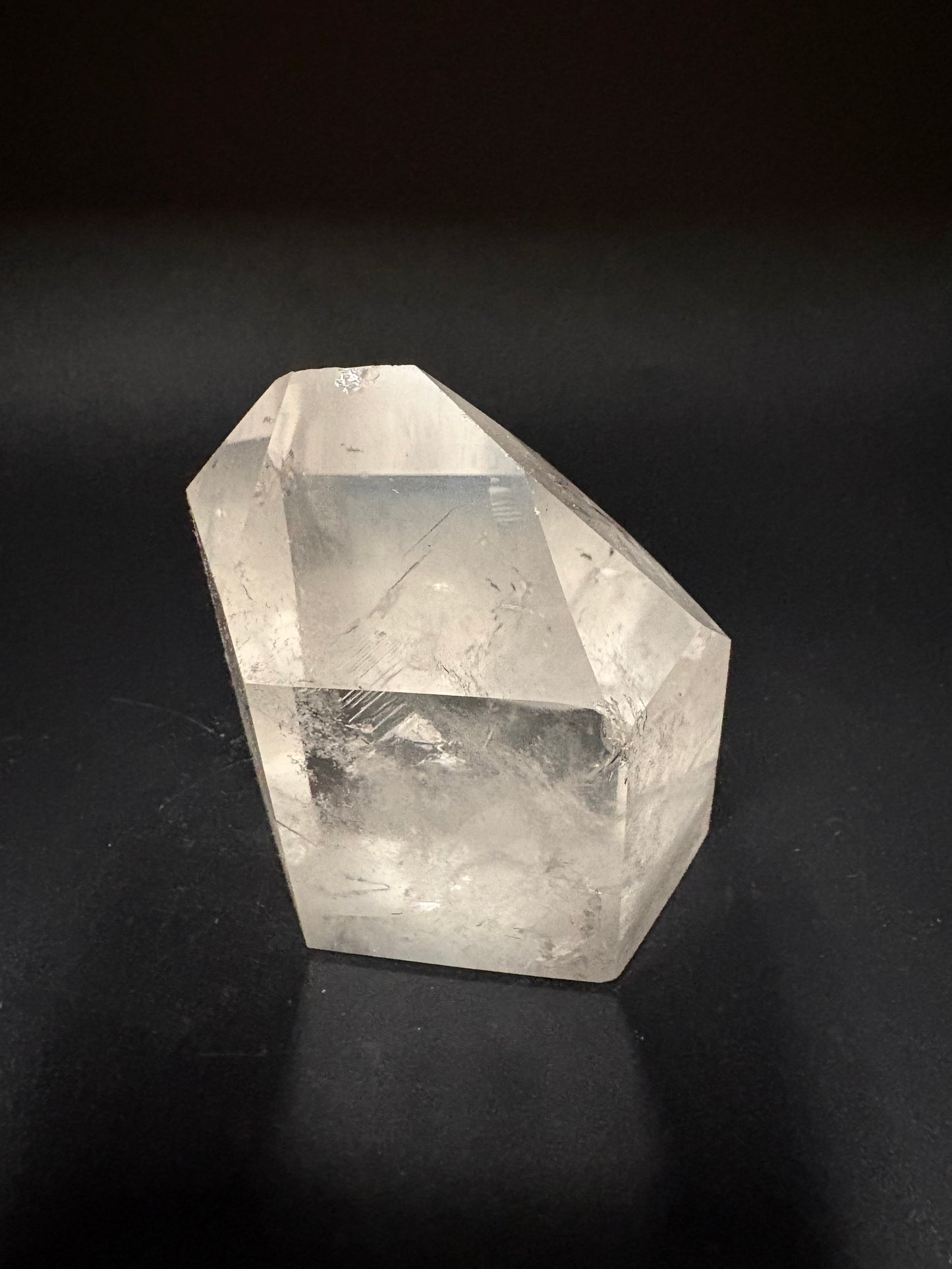 A raw, faceted clear quartz crystal point with natural inclusions, displayed on a dark black background.