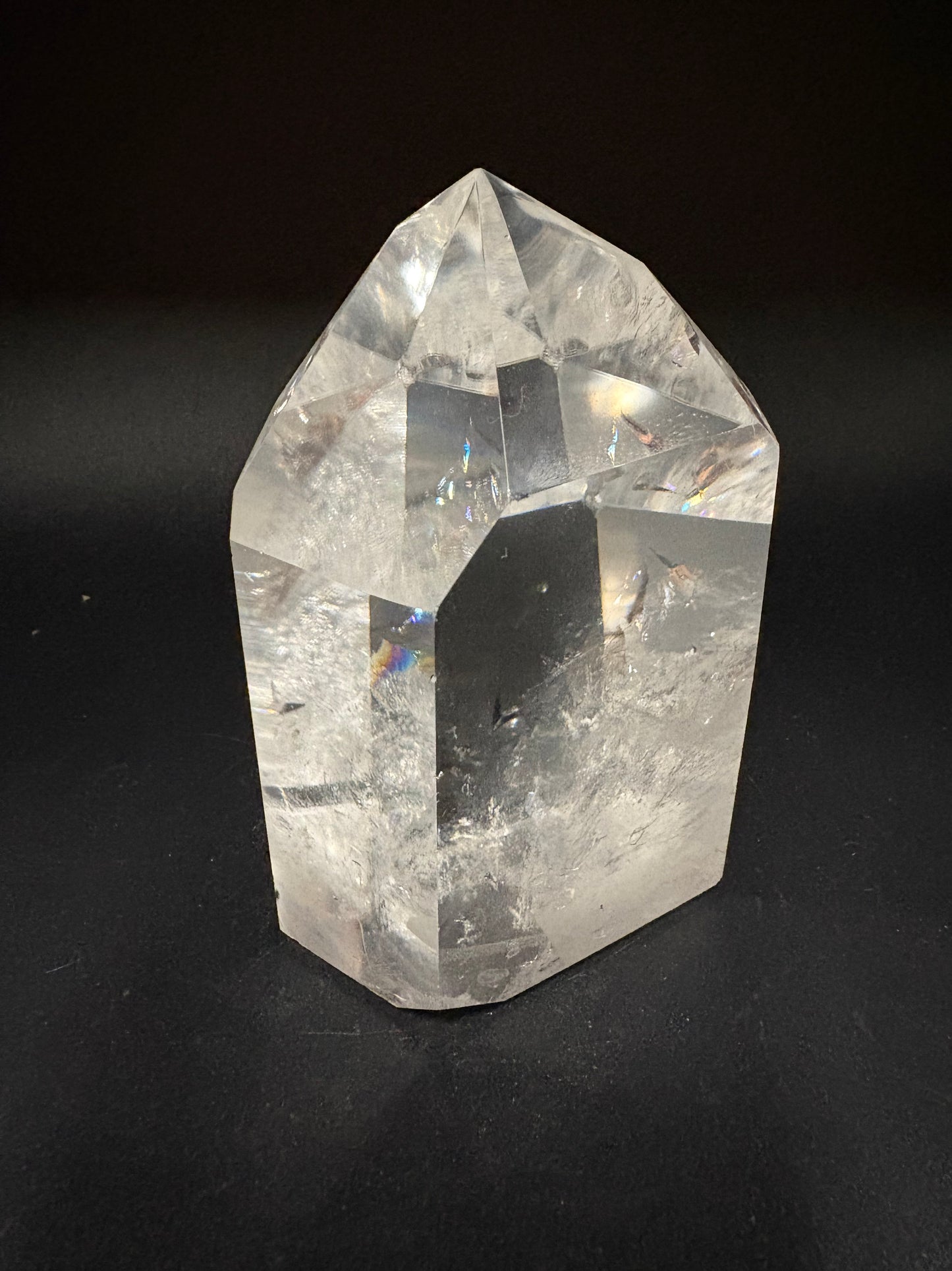 A faceted clear crystal point, likely quartz, displayed on a dark black background.