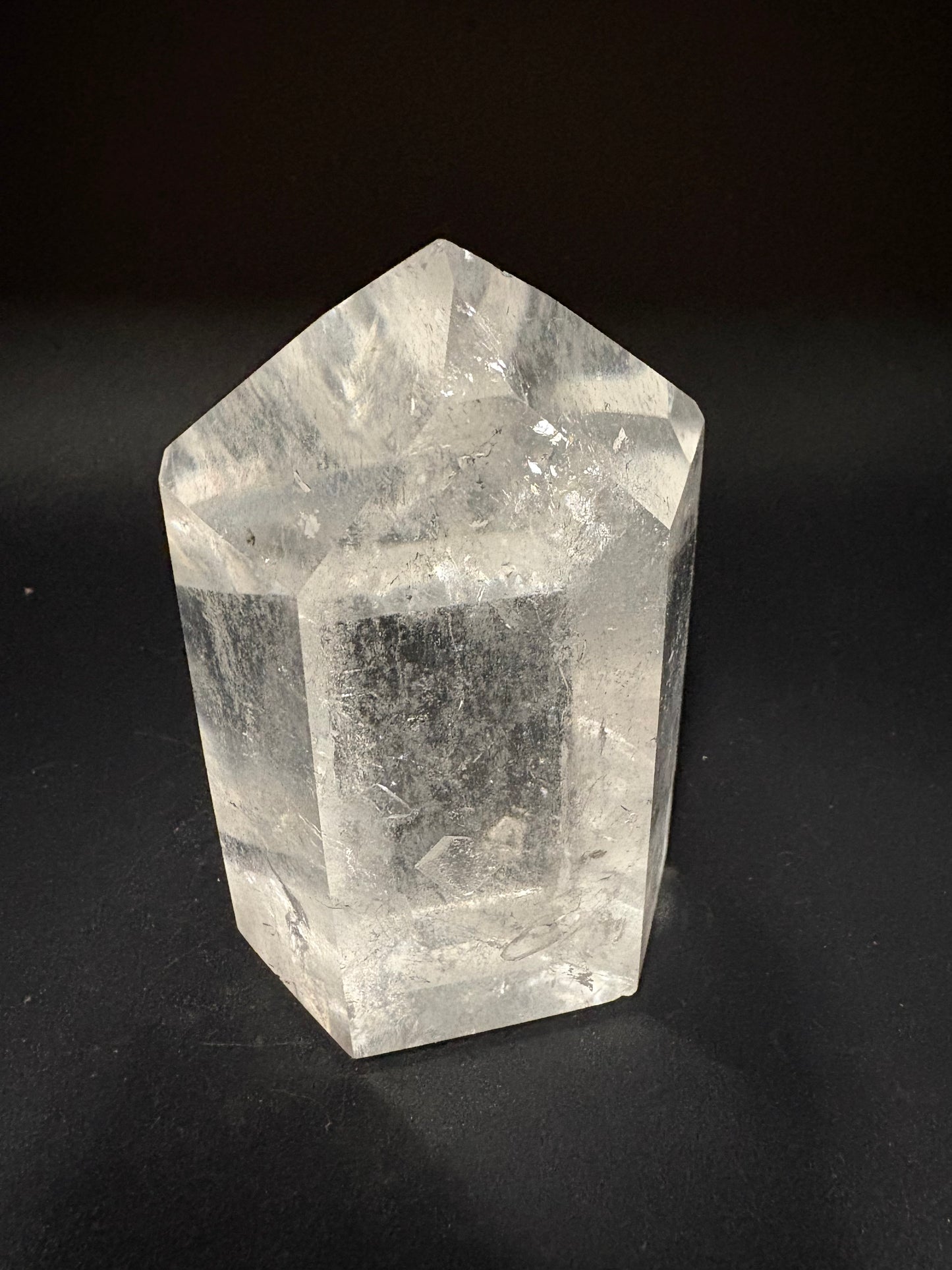A clear quartz crystal point with natural inclusions, photographed on a dark black background.