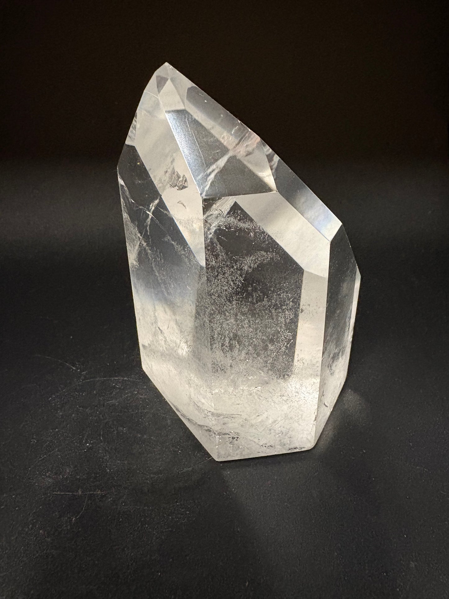 A faceted clear quartz crystal point with natural inclusions, displayed on a dark black background.