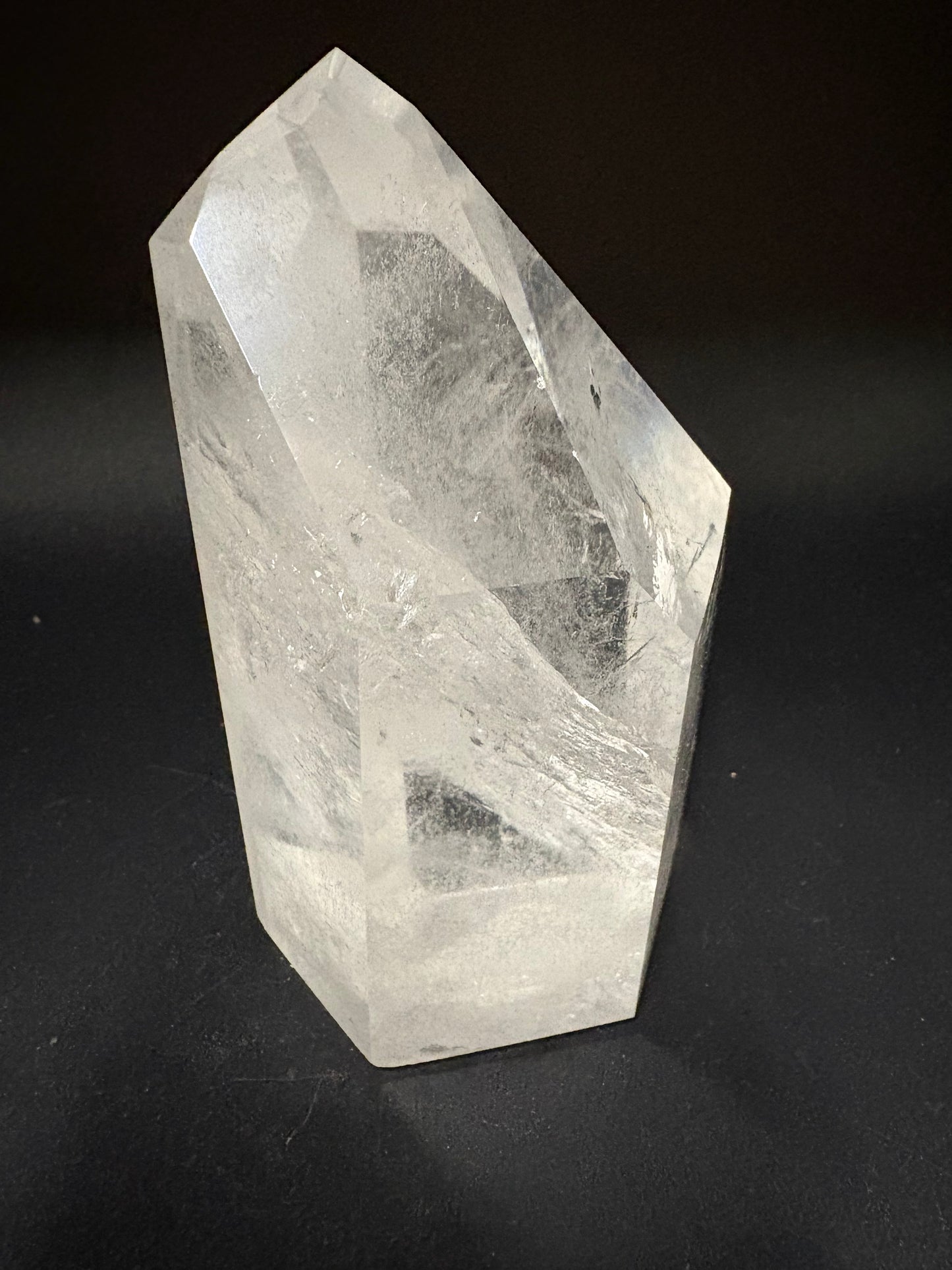 A faceted clear quartz crystal point with visible internal inclusions, photographed on a dark black background.