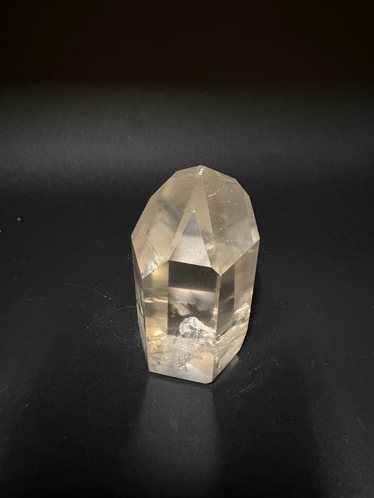 A faceted clear quartz crystal point resting on a dark, matte black surface.