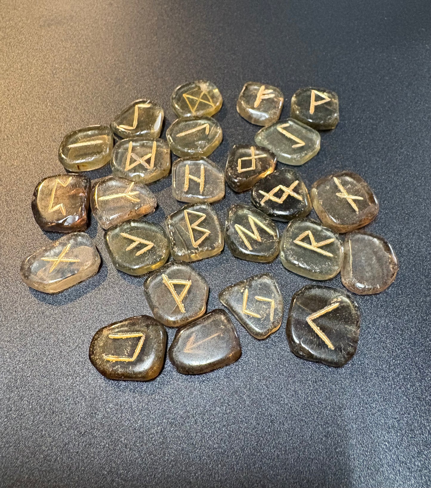 A group of polished smoky quartz stones engraved with runic symbols, arranged on a dark gray textured surface.