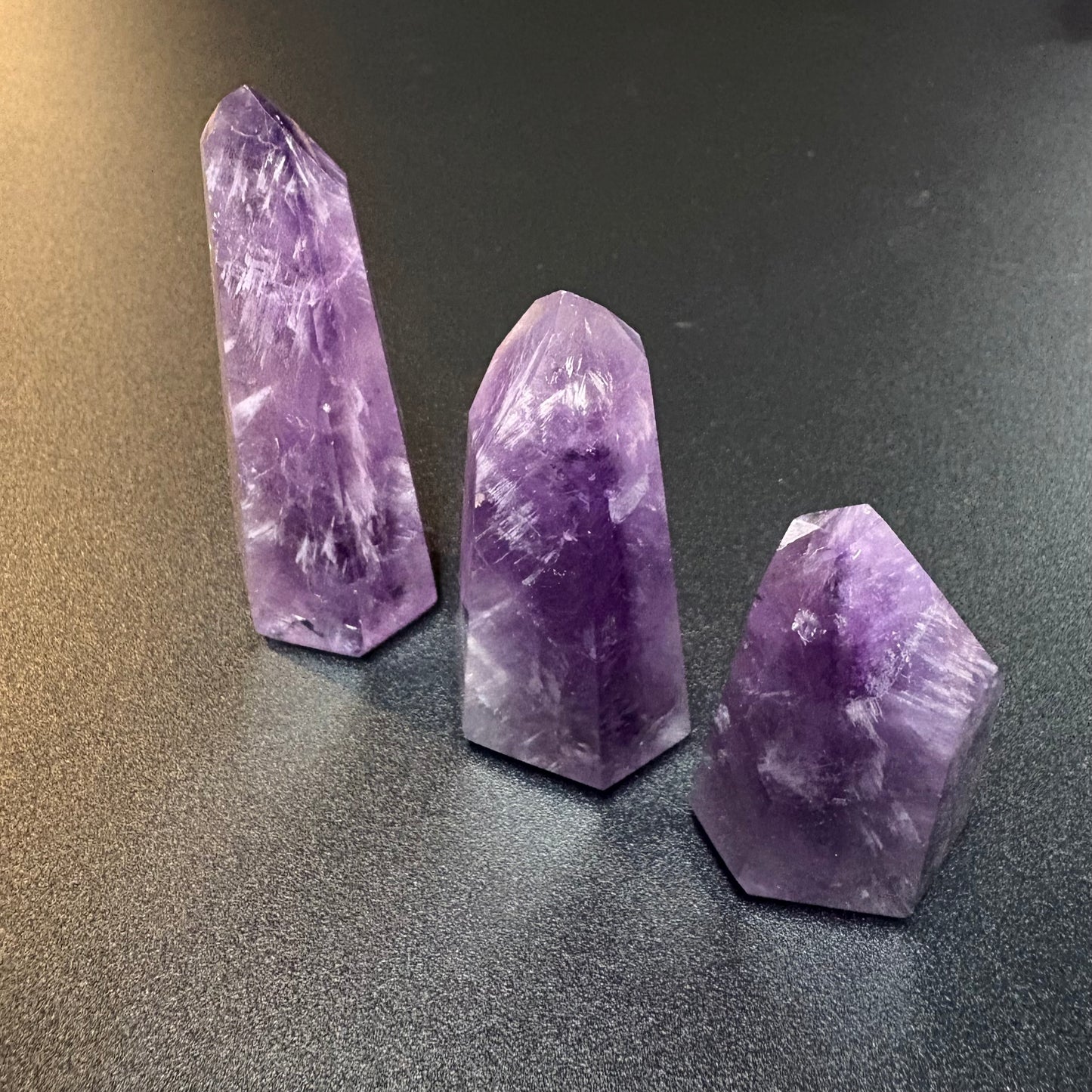 Three natural amethyst crystal points of different heights arranged on a dark gray textured surface.