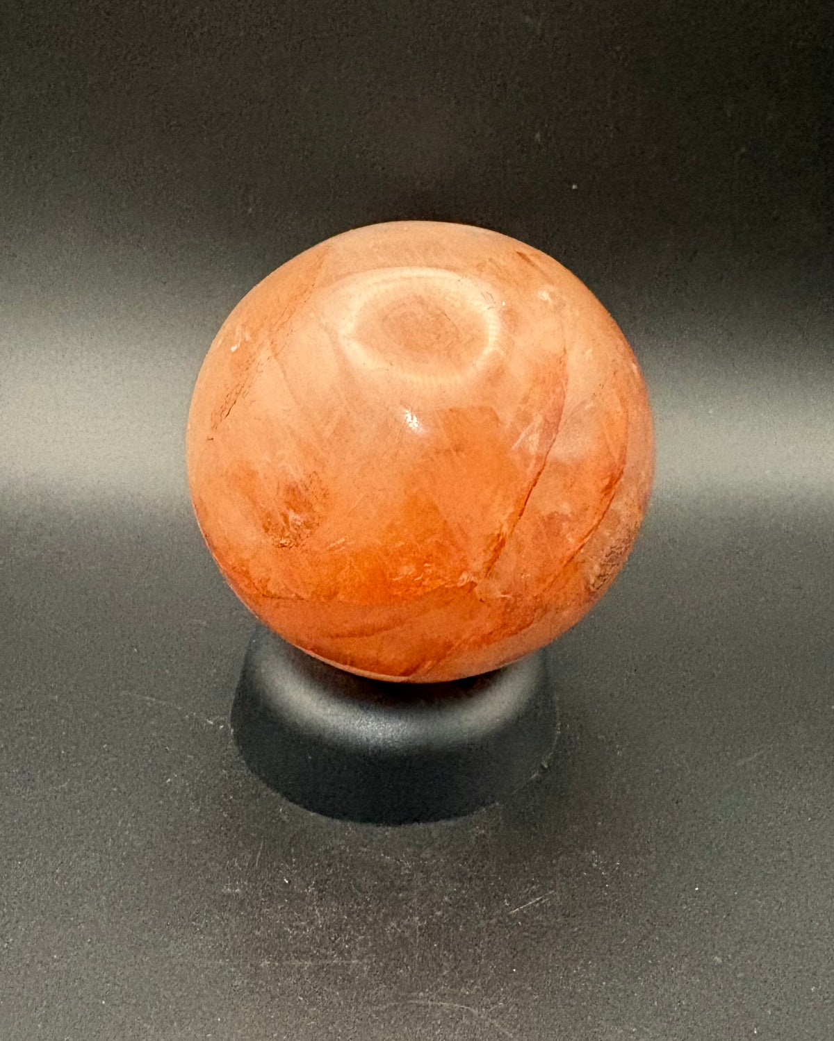 A polished Fire quartz stone sphere with natural marbling, displayed on a small black stand against a dark gray background.