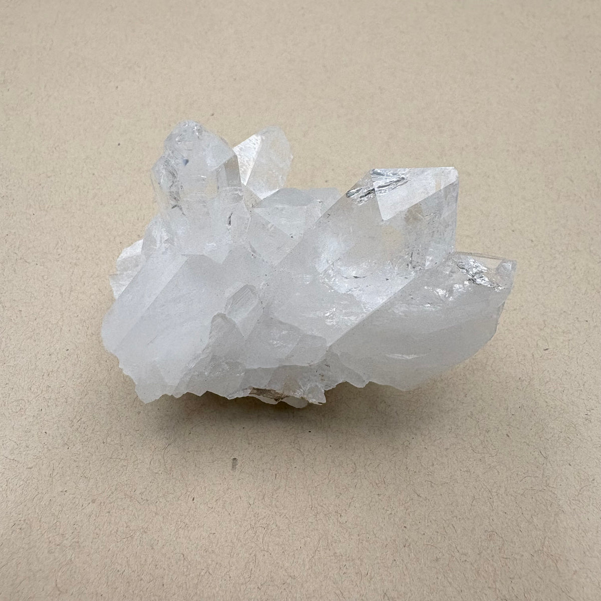A natural clear quartz crystal cluster with multiple sharp, faceted points resting on a textured beige surface.