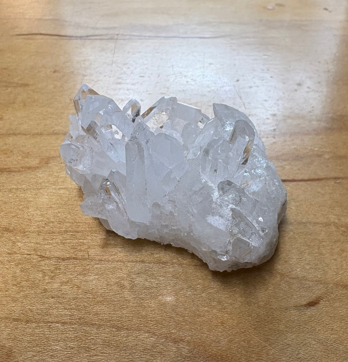 A raw quartz crystal cluster with multiple clear, faceted points resting on a light brown wooden surface.