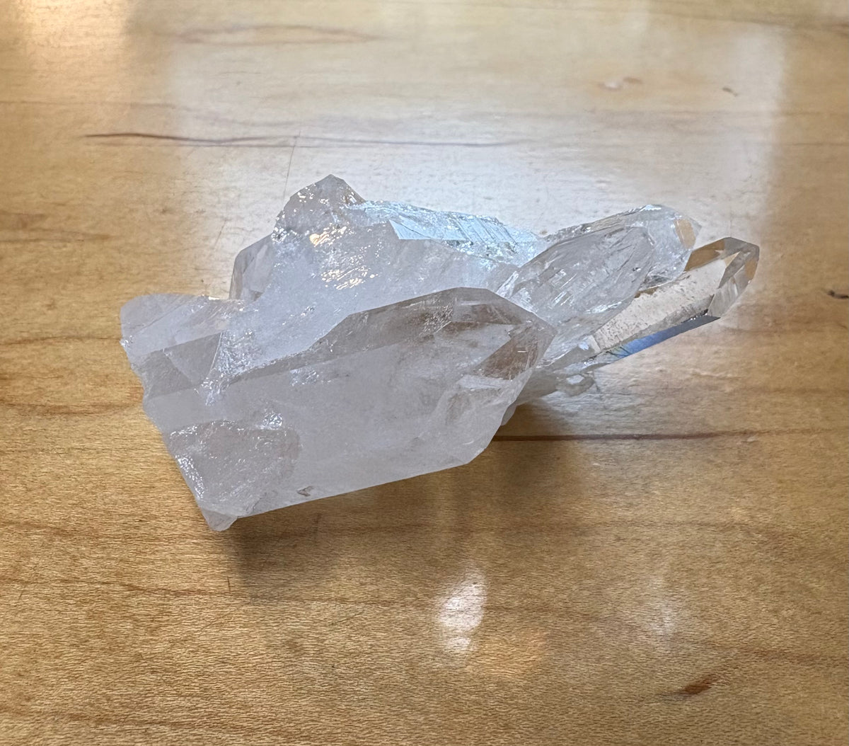 A raw, unpolished clear quartz crystal cluster with natural jagged points, resting on a light brown wooden tabletop.
