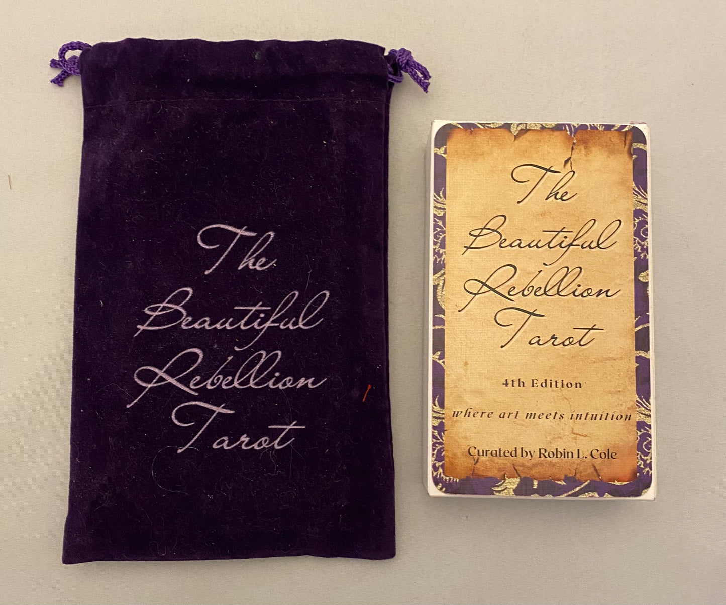 Purple velvet bag and 'The Beautiful Rebellion Tarot' packaging on a light gray background