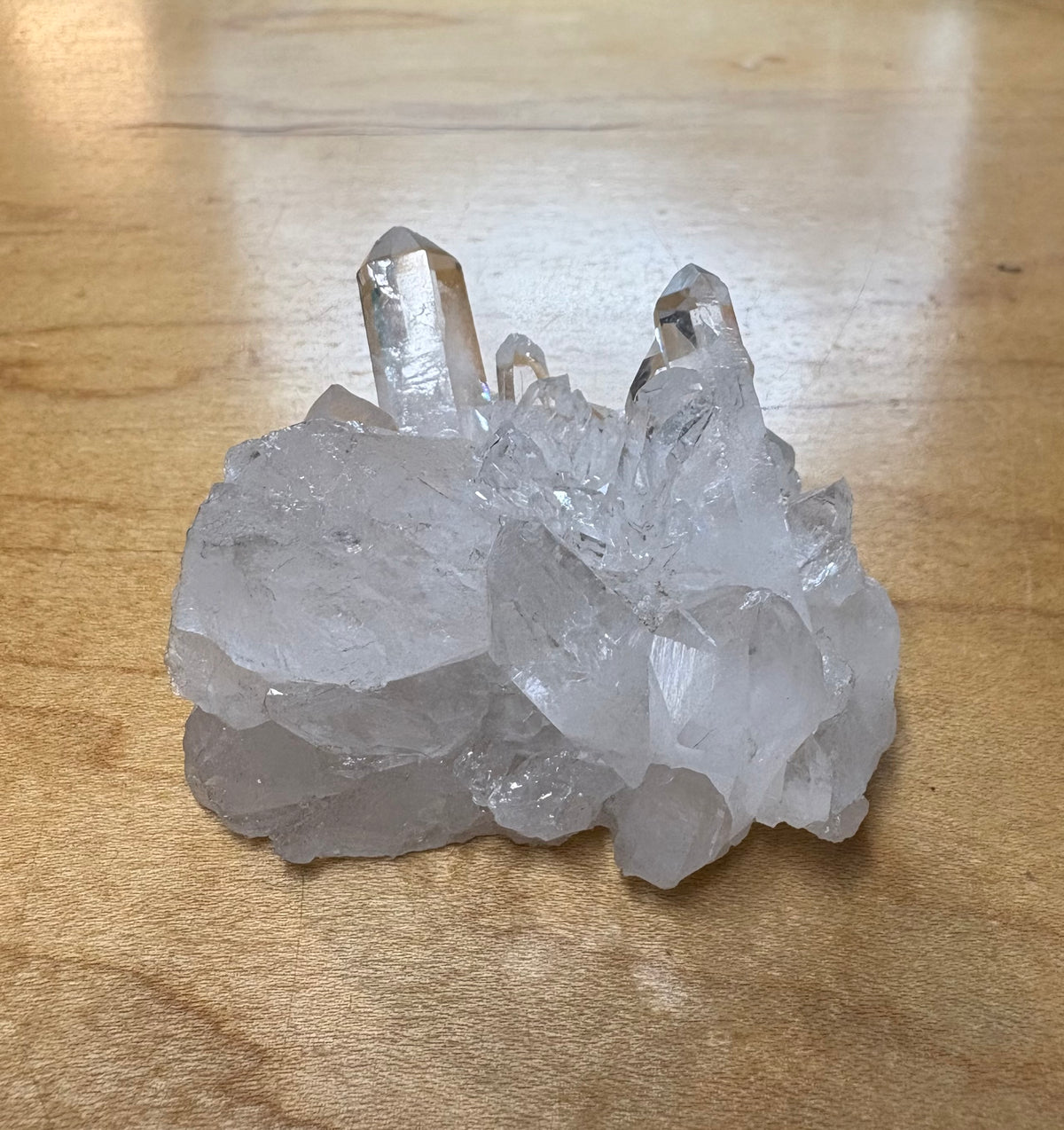 A cluster of natural clear quartz crystals with multiple pointed tips, resting on a light brown wooden surface.
