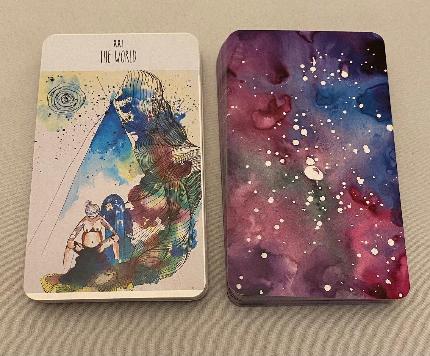Two tarot cards, one with a colorful illustration and the other with a starry night design, on a neutral background.