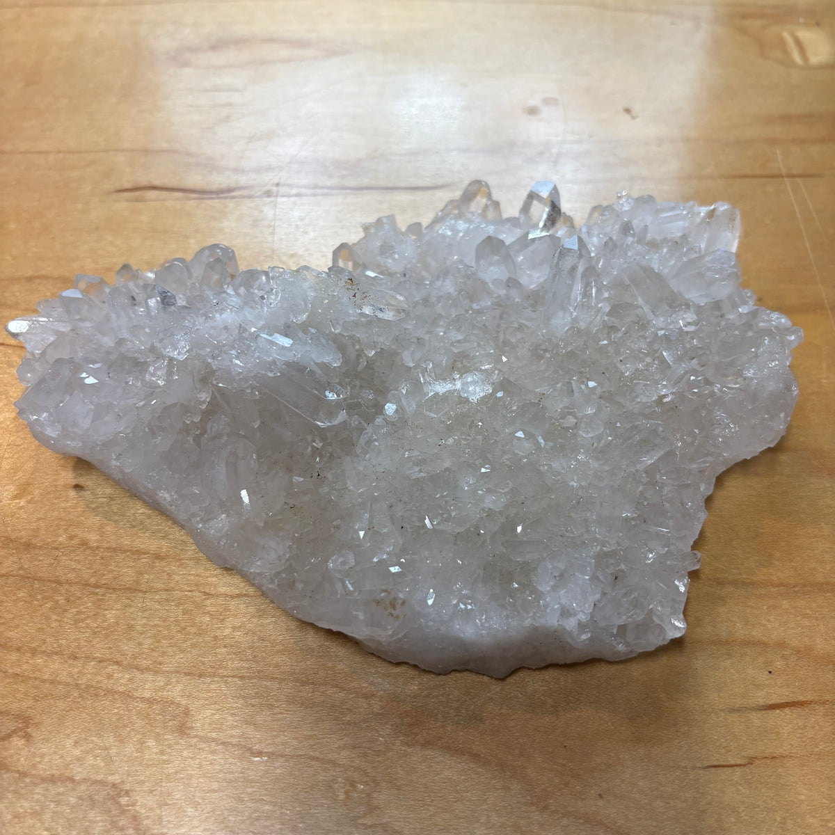 A raw crystal cluster with clear, faceted quartz-like points resting on a light brown wooden surface.