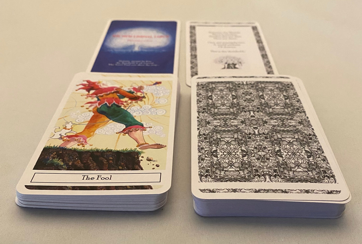 Two tarot cards on a light gray surface, one with an illustration of a person labeled 'The Fool' and the other with a black and white pattern.