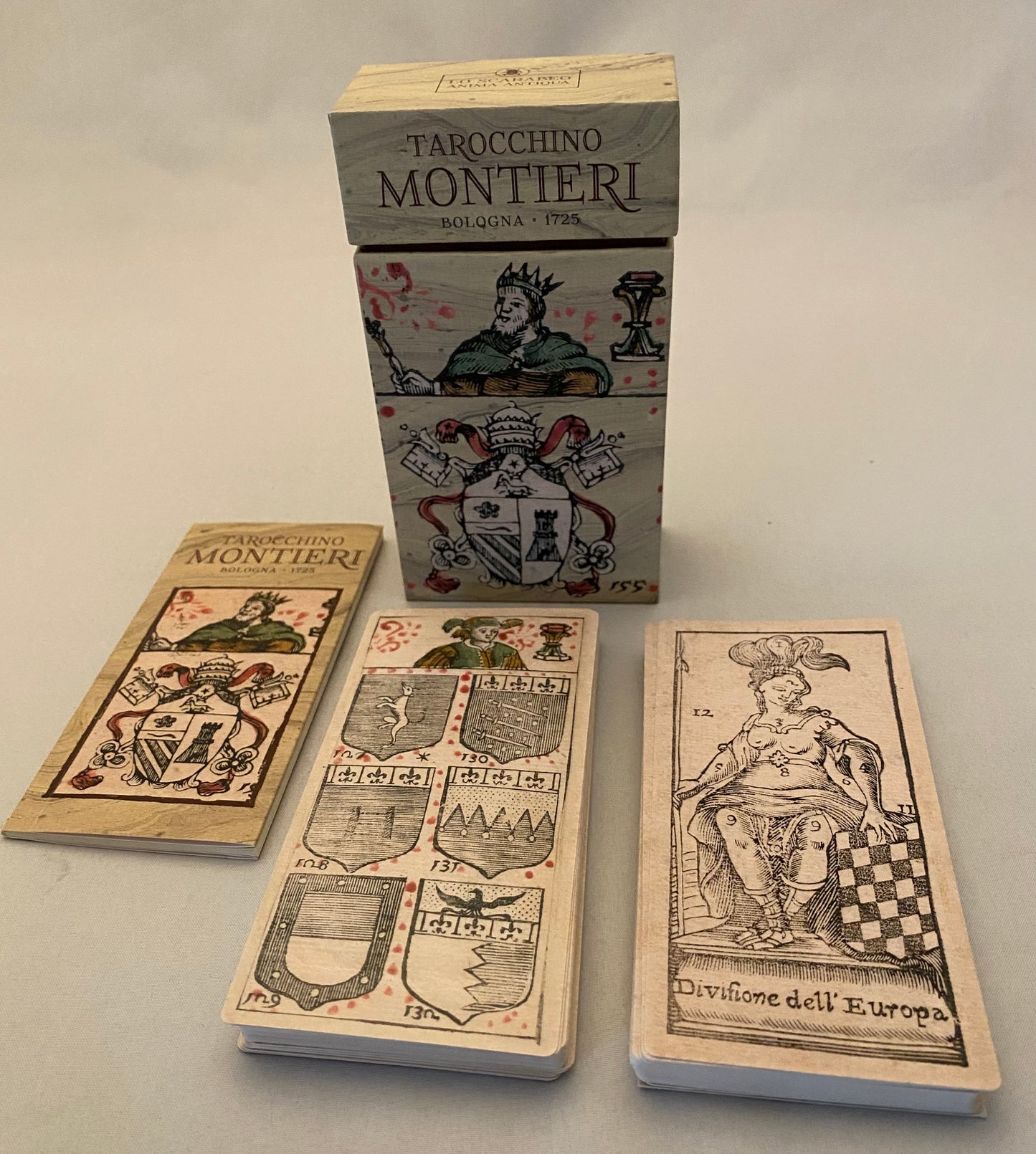 tarot cards with intricate designs and a box labeled 'Tarocchino Montieri' on a light gray background.
