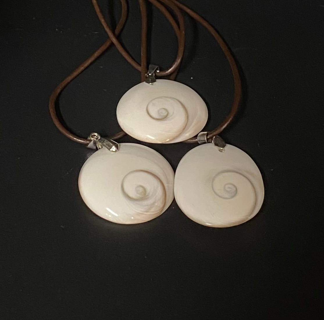 Necklace with three white spiral shell pendants on a dark background