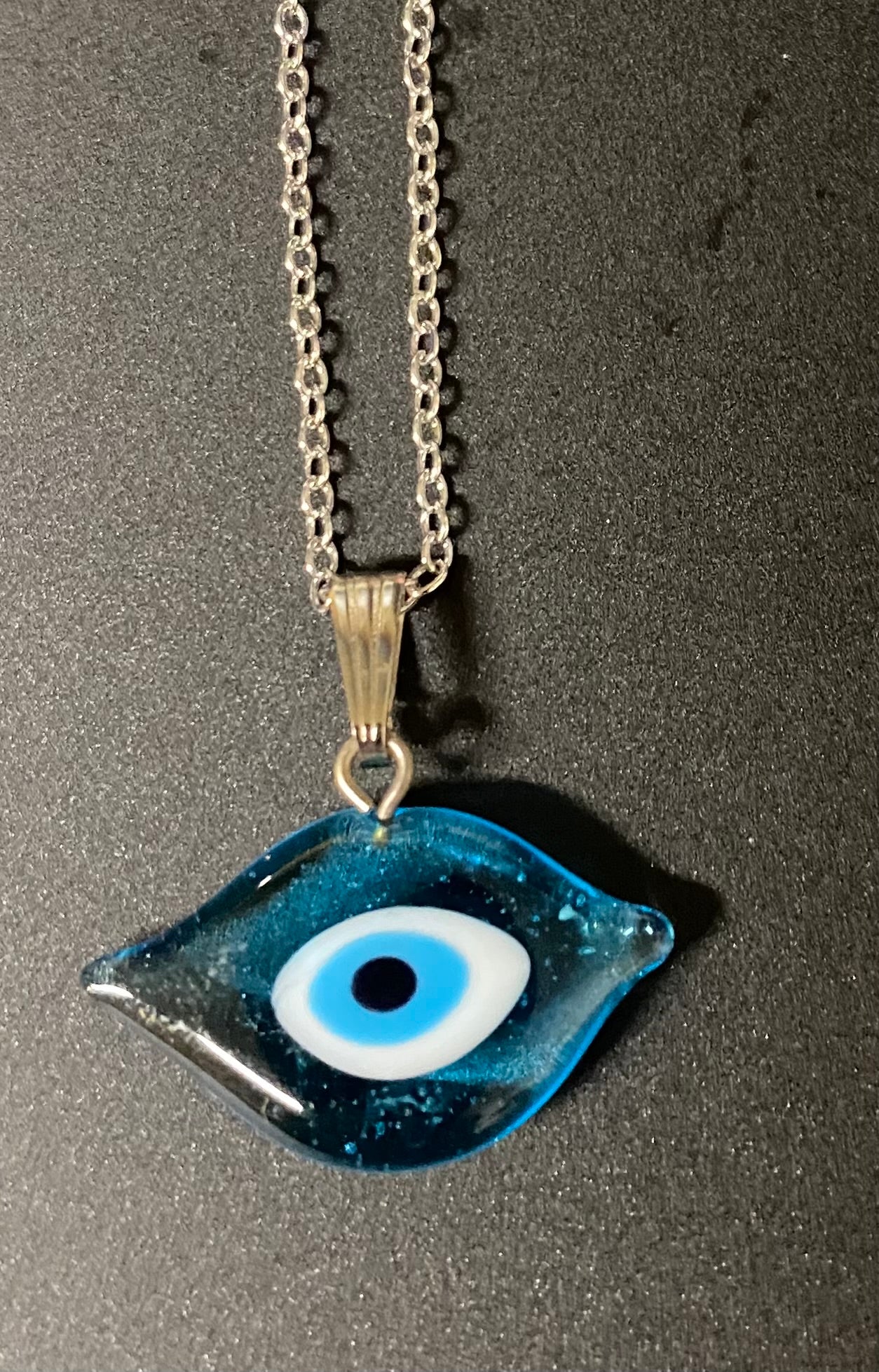 Blue eye-shaped pendant on a chain against a dark background