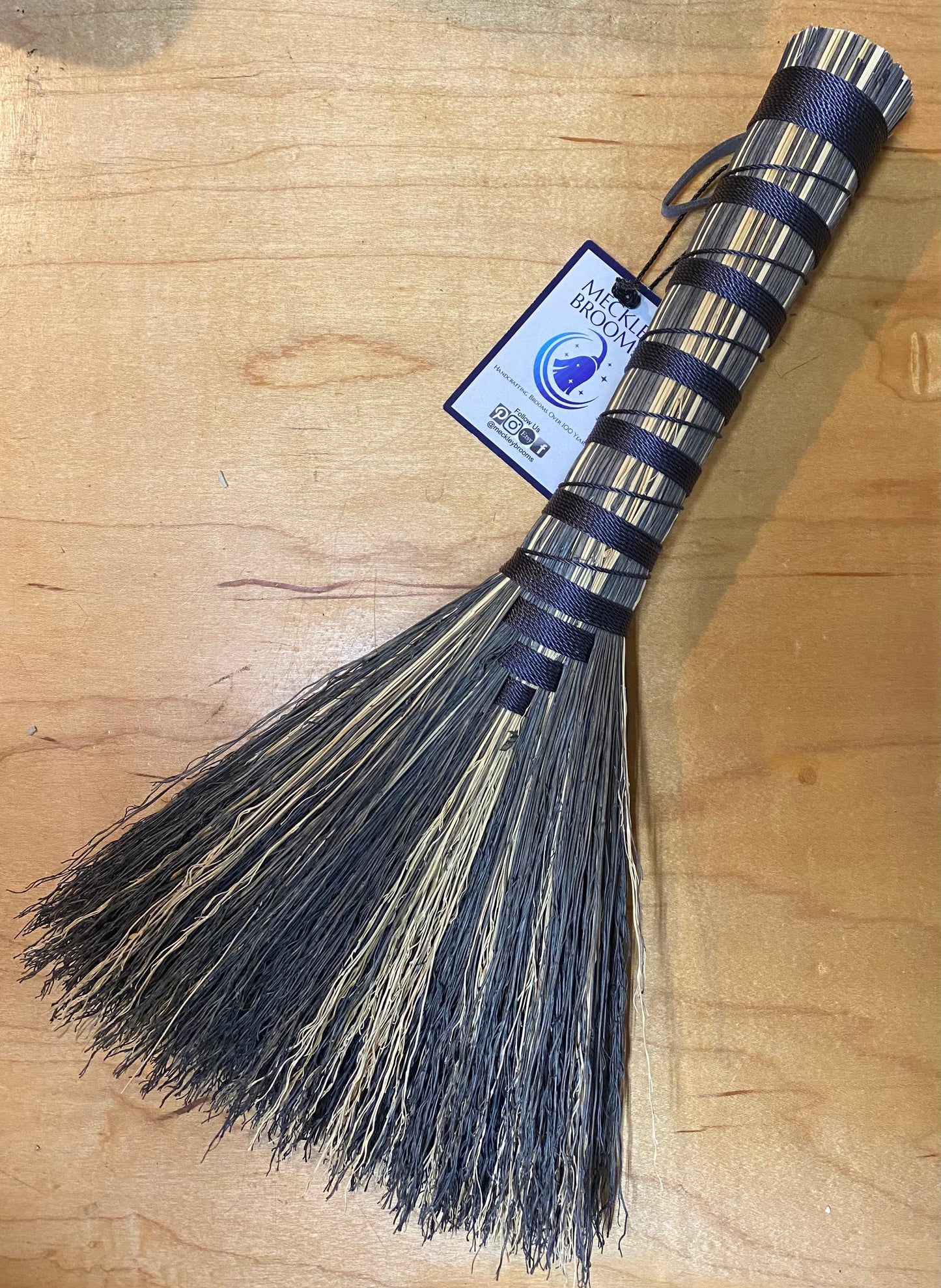 Broom with a blue handle and bristles on a wooden surface, featuring a brand tag.