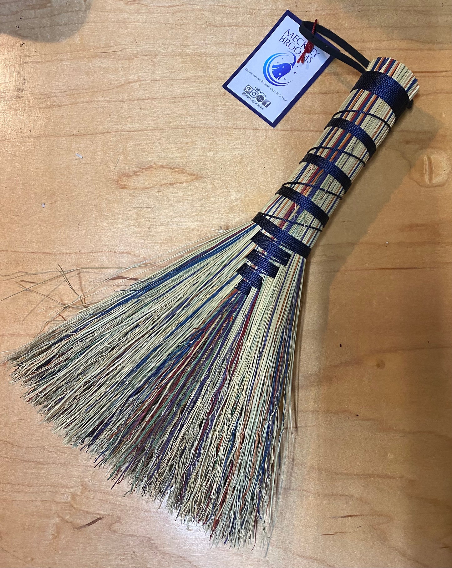 Broom with a blue handle and bristles on a wooden surface, featuring a label.