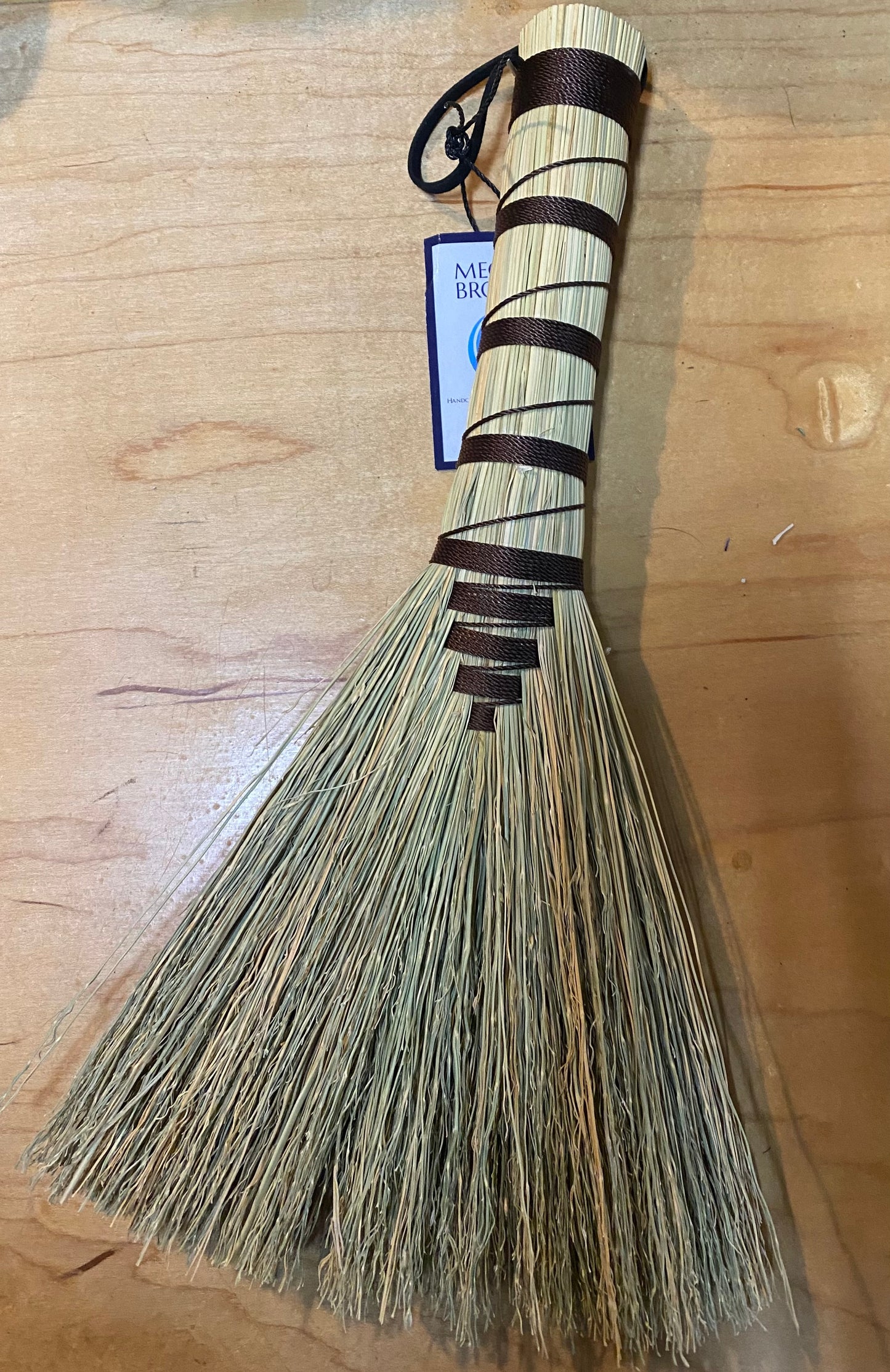Handheld broom with black handle and bristles on a wooden surface
