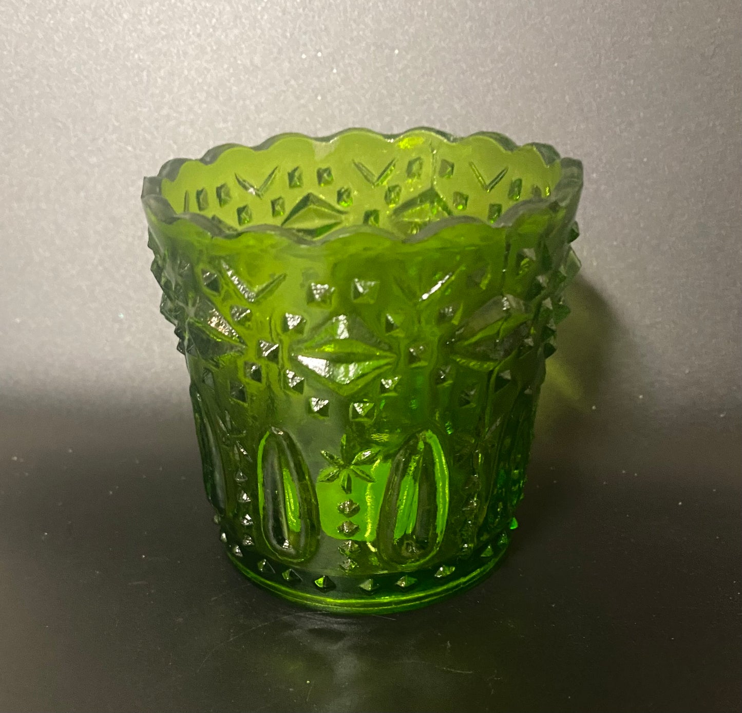 Green glass candle holder with textured design on a reflective surface