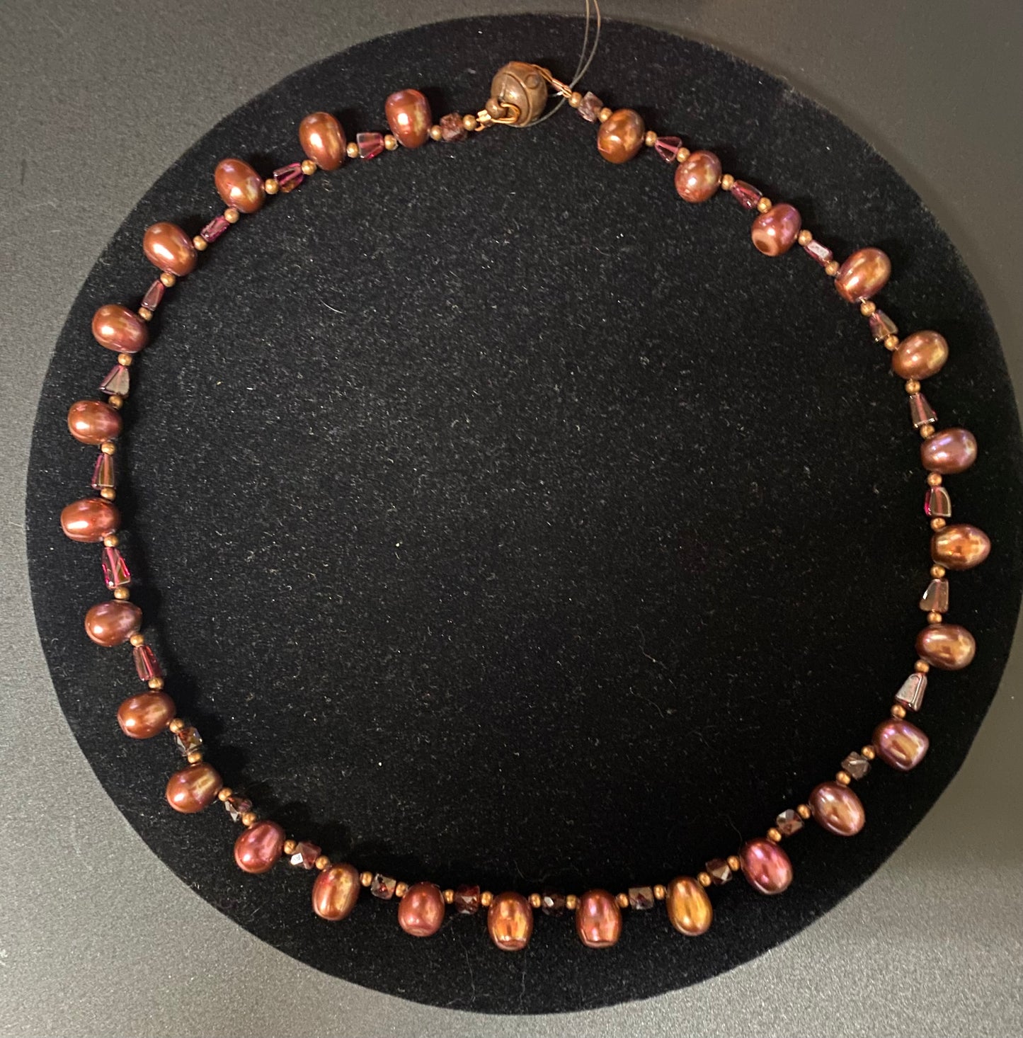 Necklace with brown and pink beads on a black circular stand