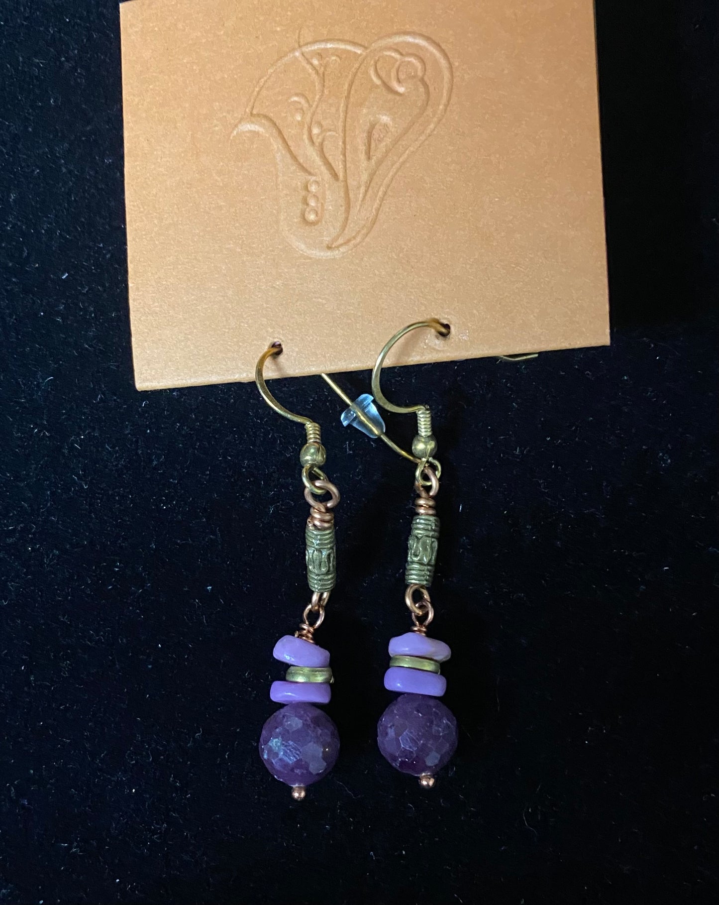 Pair of purple beaded earrings on a dark background with a brand card.
