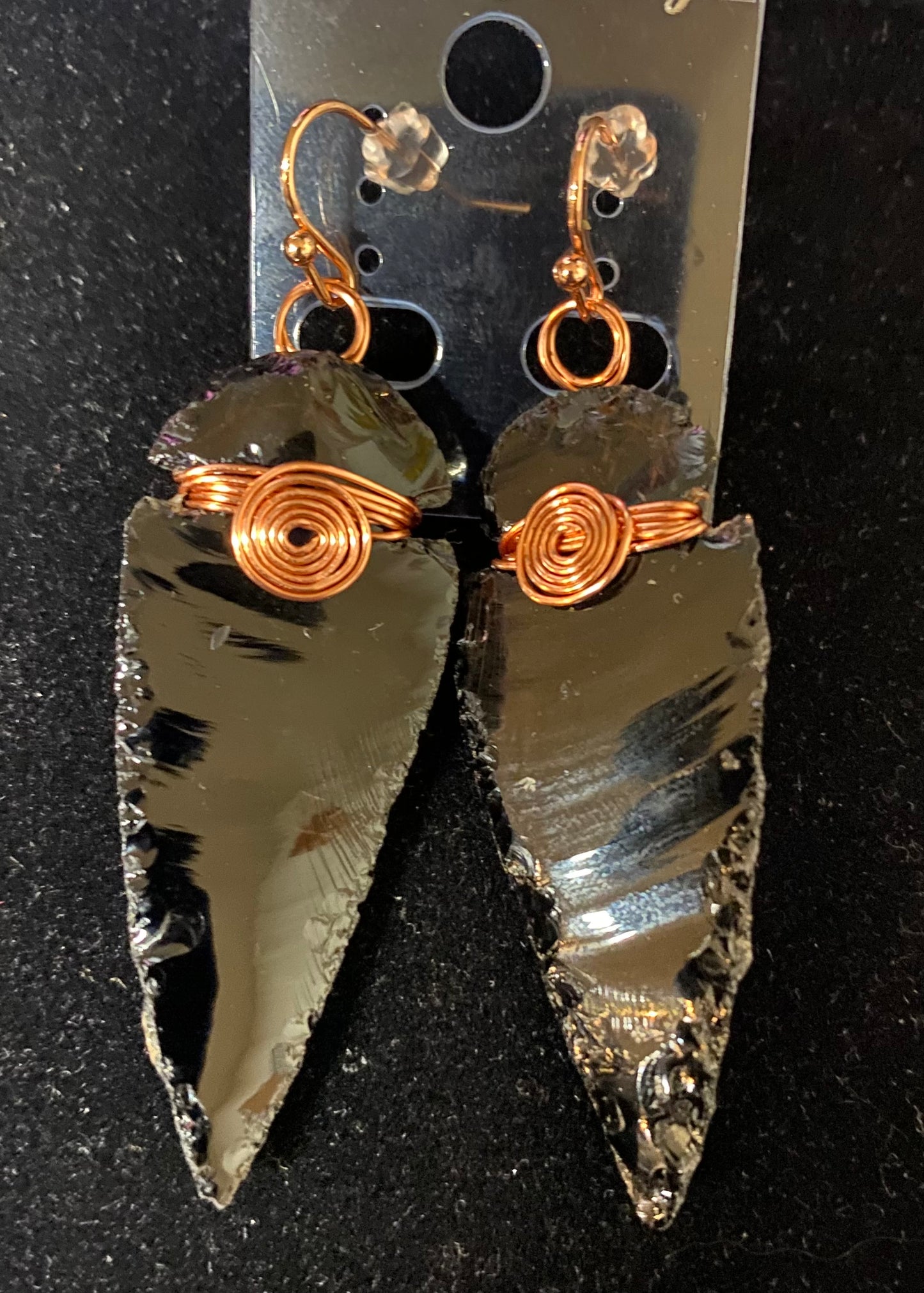 Arrowhead-shaped earrings with copper wire wrapping on a black background