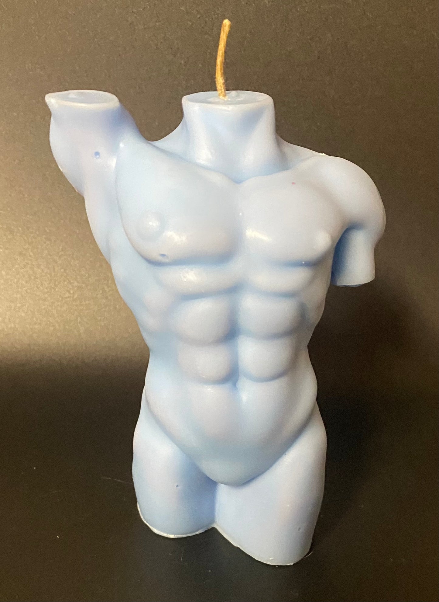 Candle shaped like a muscular torso on a dark background