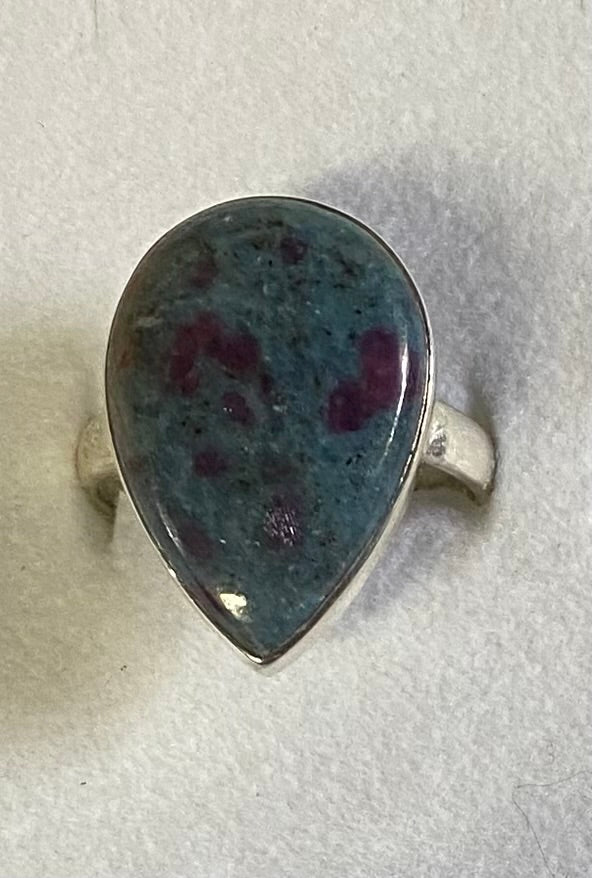 Teardrop-shaped ring with a blue and red speckled stone on a light gray background