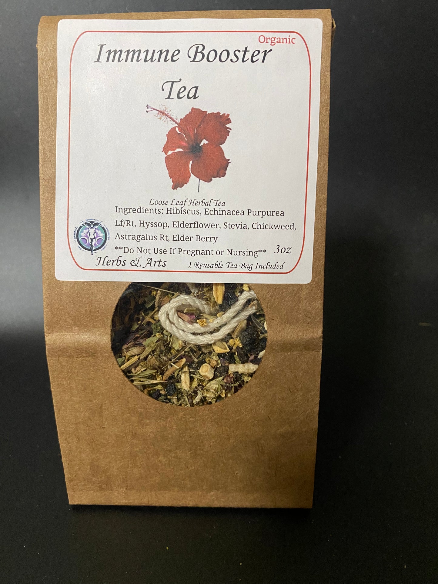 A stand-up kraft paper pouch of Immune Booster Tea with a white label and a circular window showing the dried herbal tea inside, photographed against a dark background.